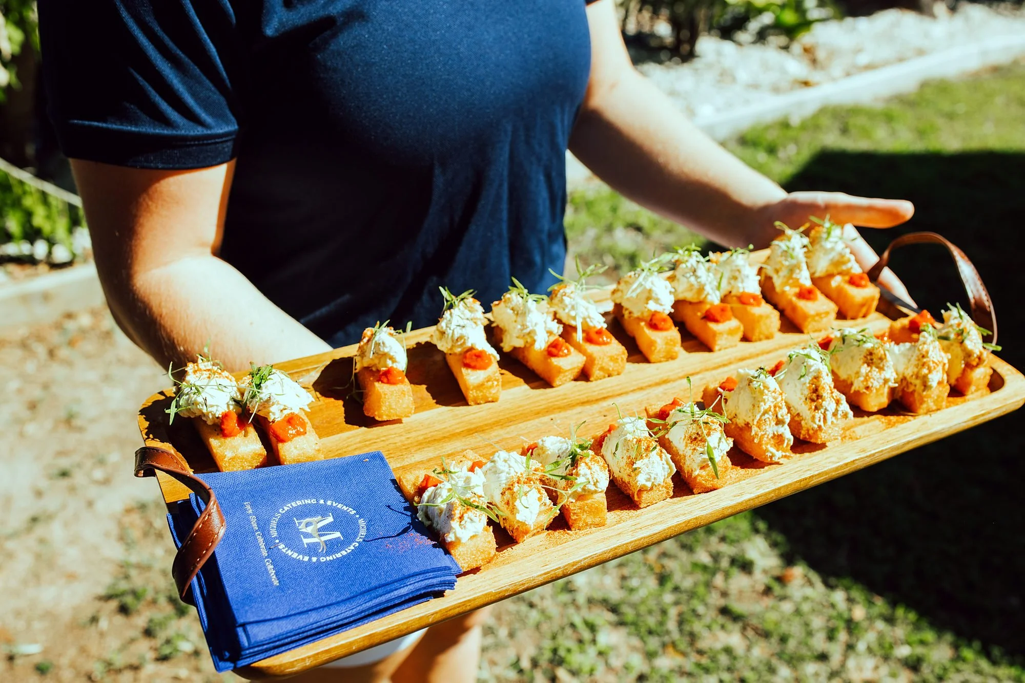 Michels staff member carrying a long board of canapés at an outdoor event