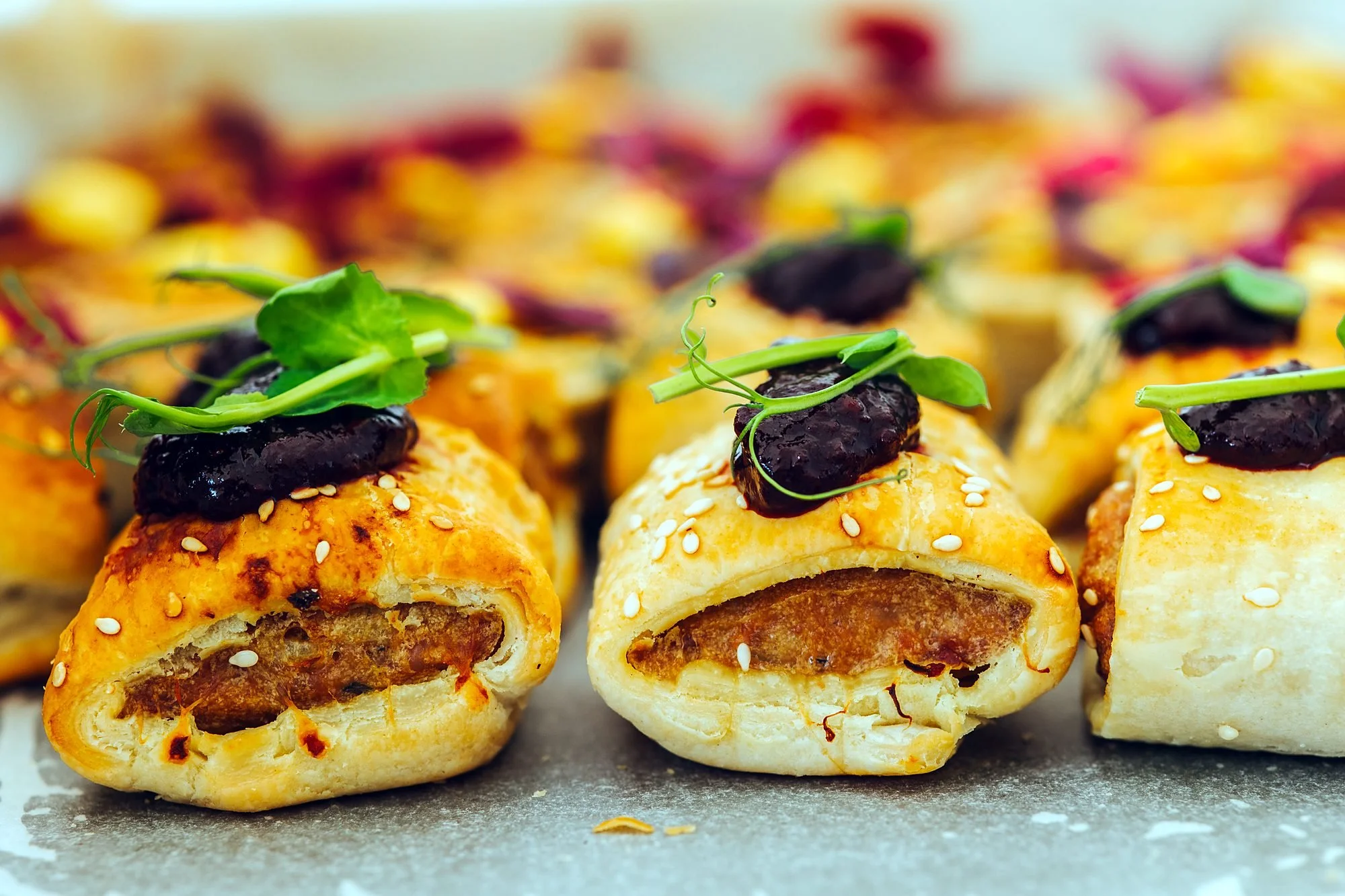 Golden sausage roll canapés topped with relish and micro herbs