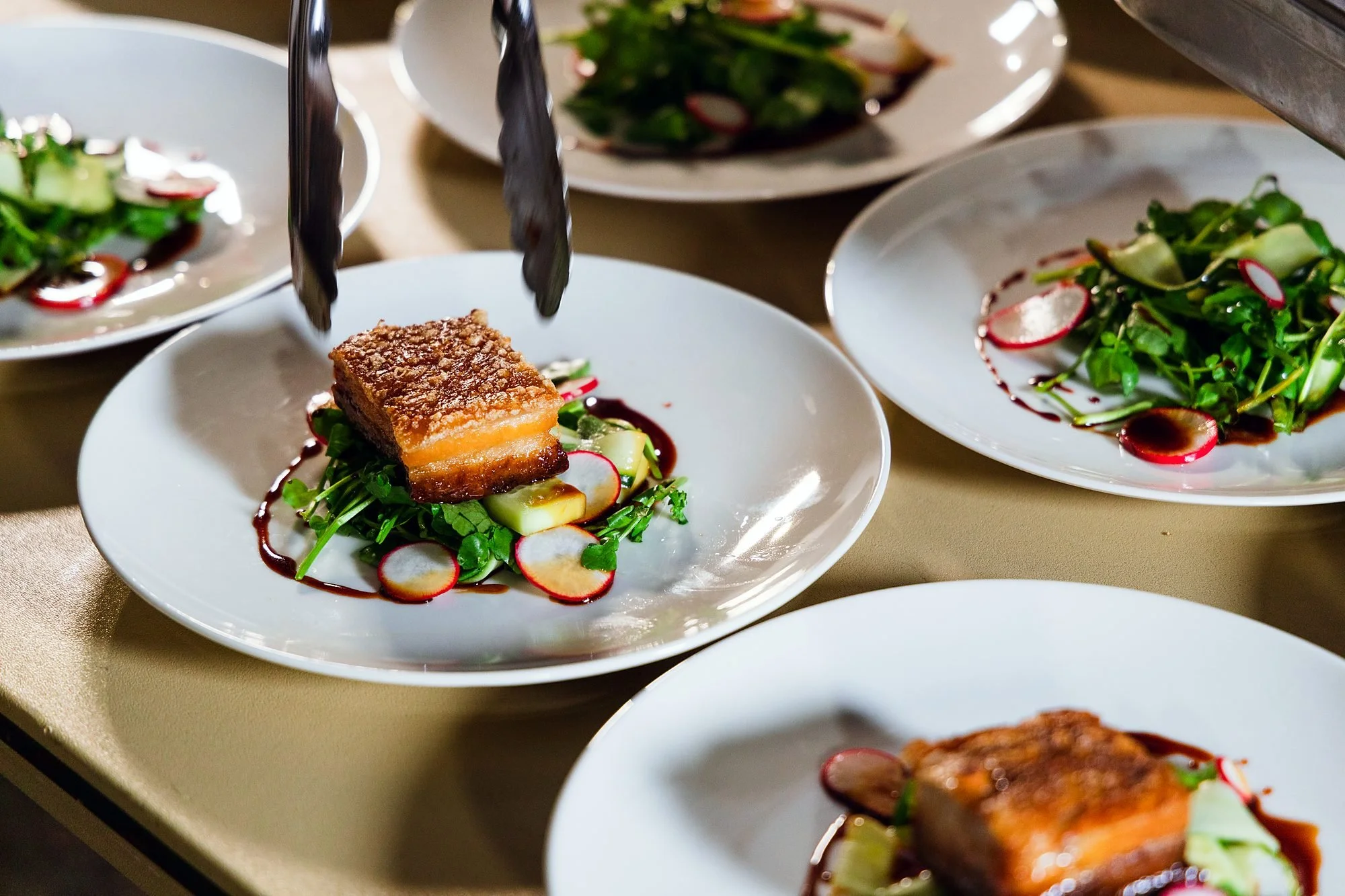 Chef plating crispy pork belly with radish and greens for a wedding main course