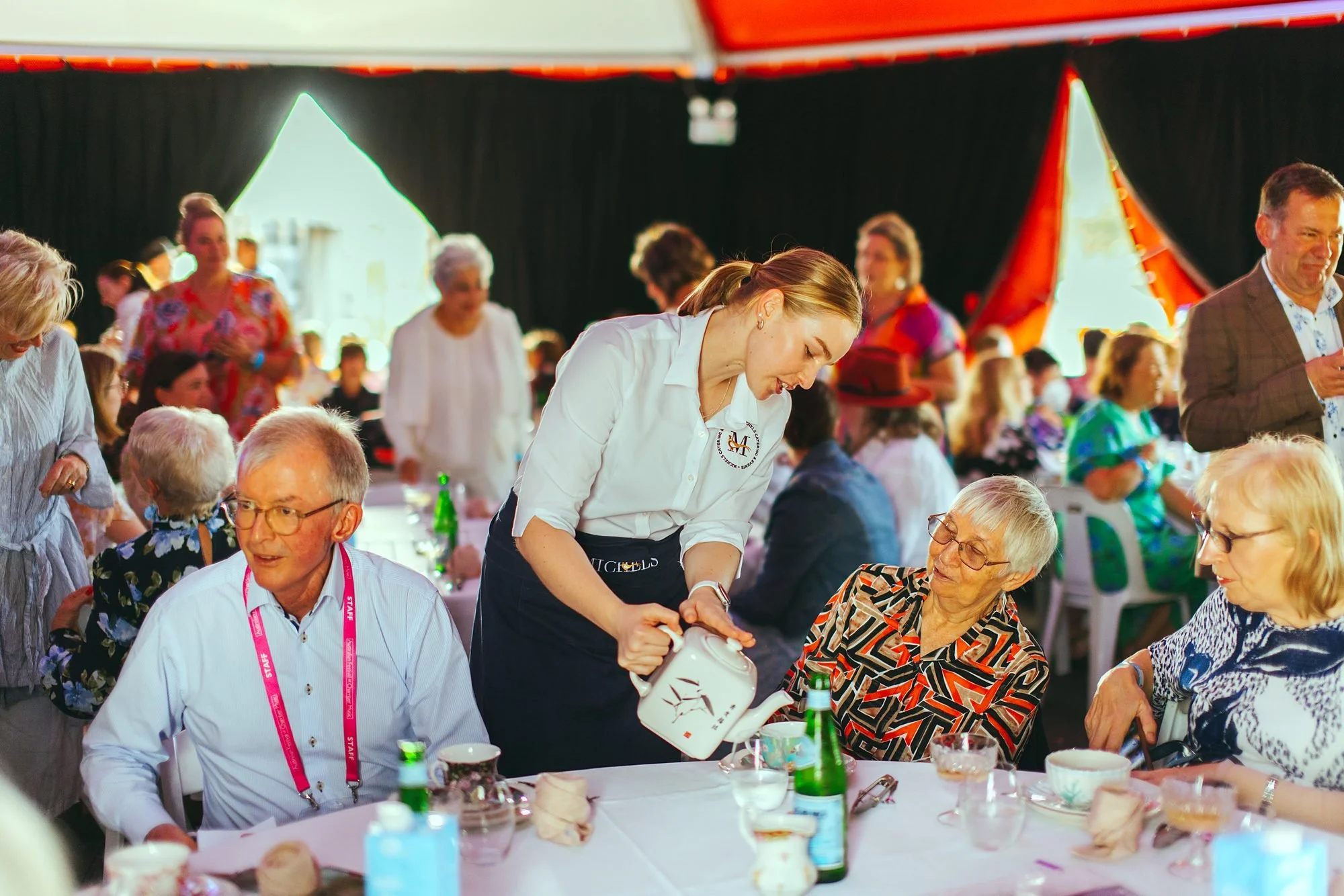 Michels staff serving tea to a full marquee of guests at a large luncheon