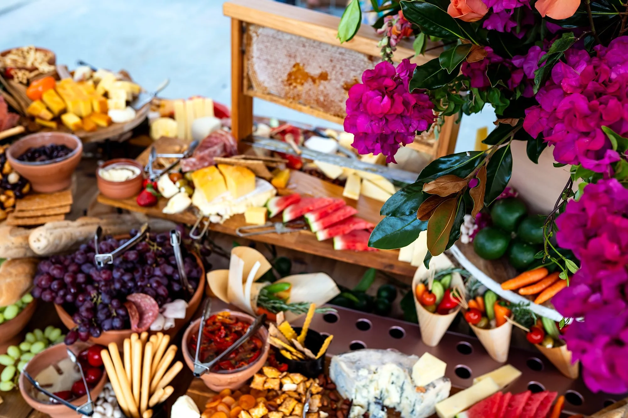 Abundant grazing table of cheeses, charcuterie and fruit styled with bright bougainvillea