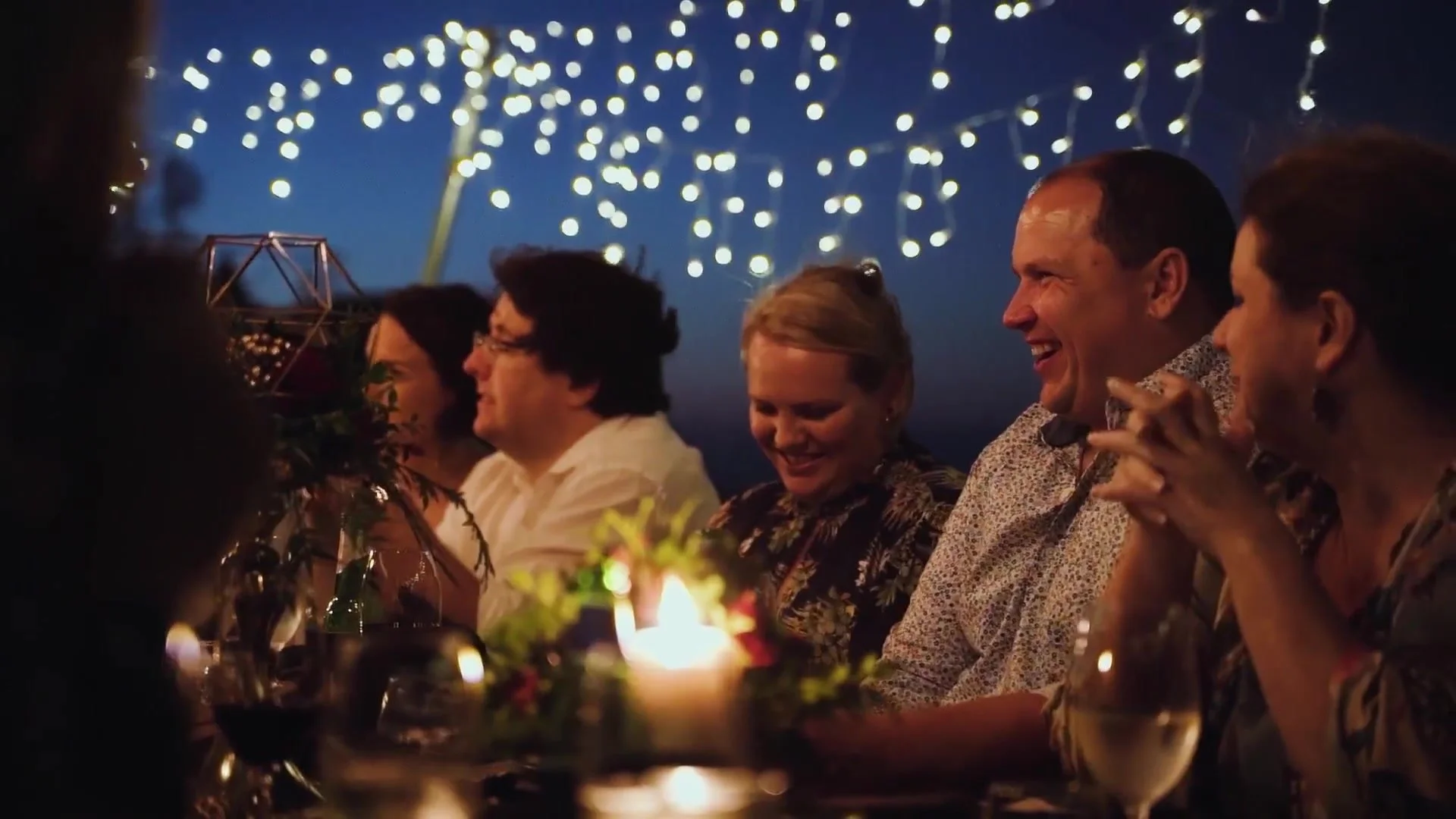 Guests laughing at a candlelit dinner under festoon lights.jpg