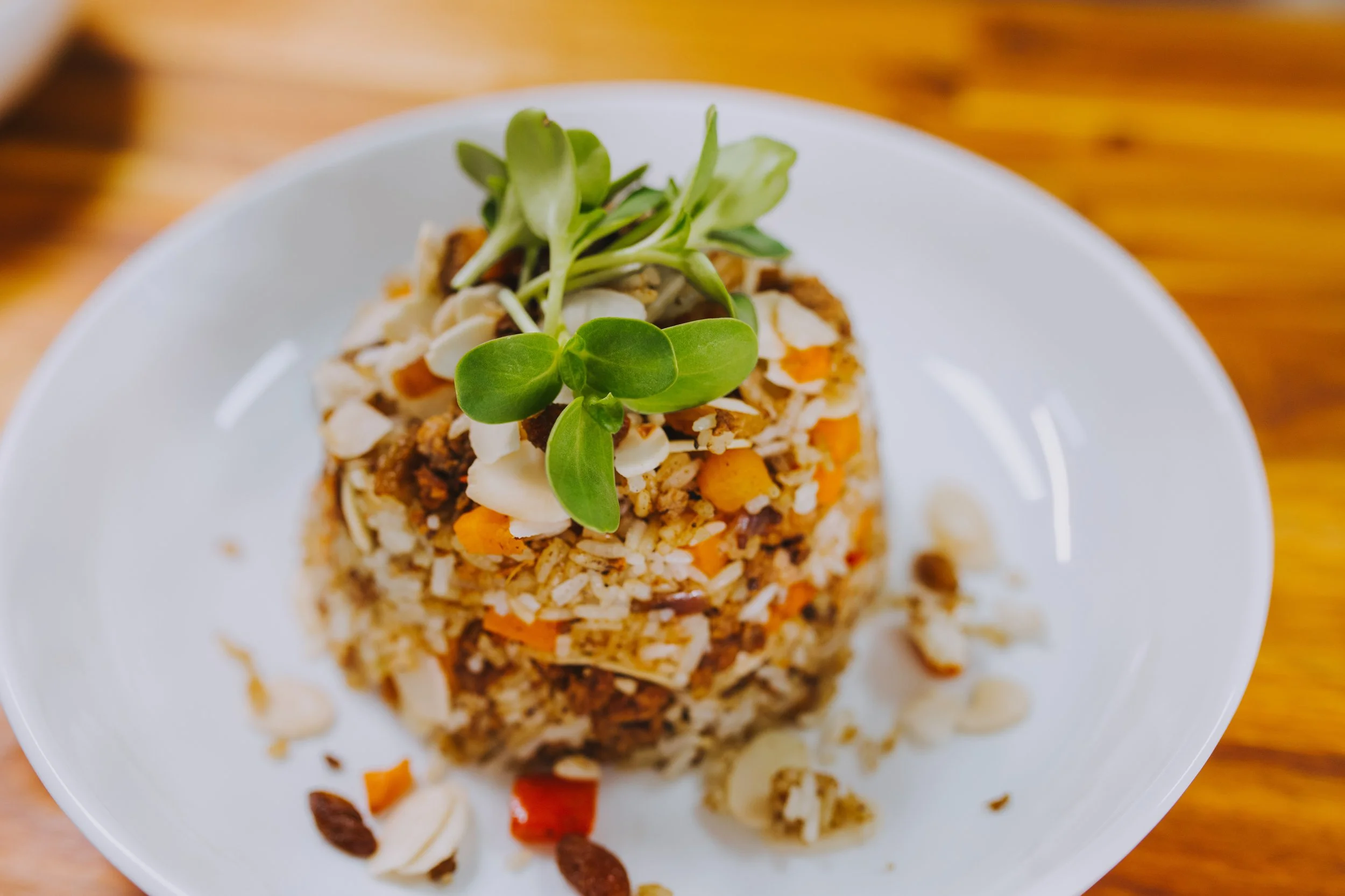 A white plate with a serving of rice and vegetables topped with fresh microgreens on a wooden table.