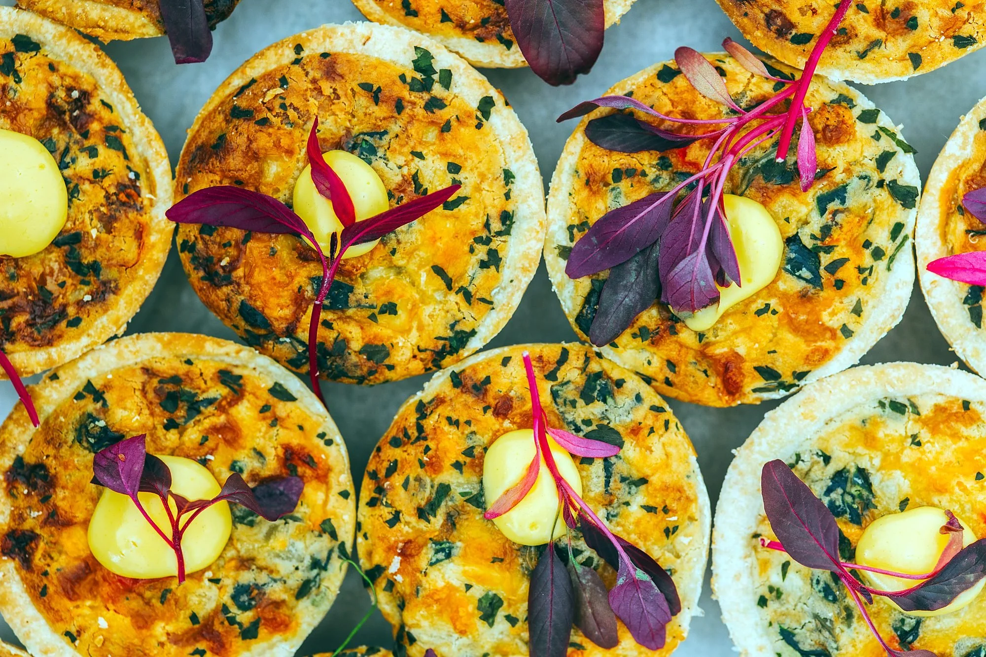 Savoury tartlets garnished with herbs and beetroot leaves on a catering platter