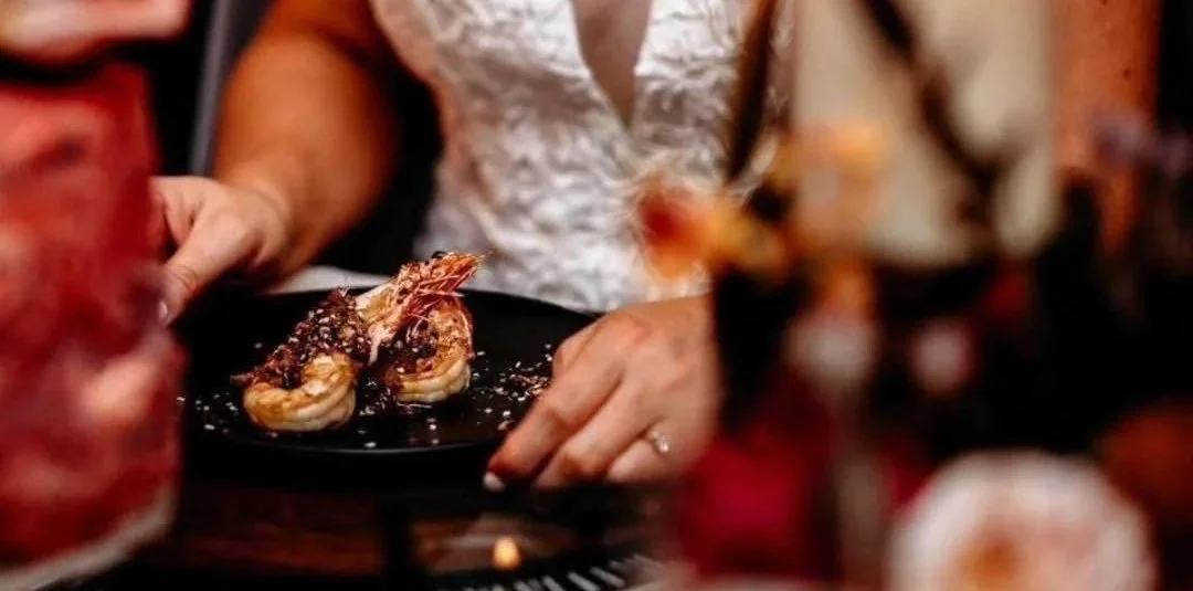 Person serving shrimp dish at a restaurant, with grilled shrimp on a black plate.