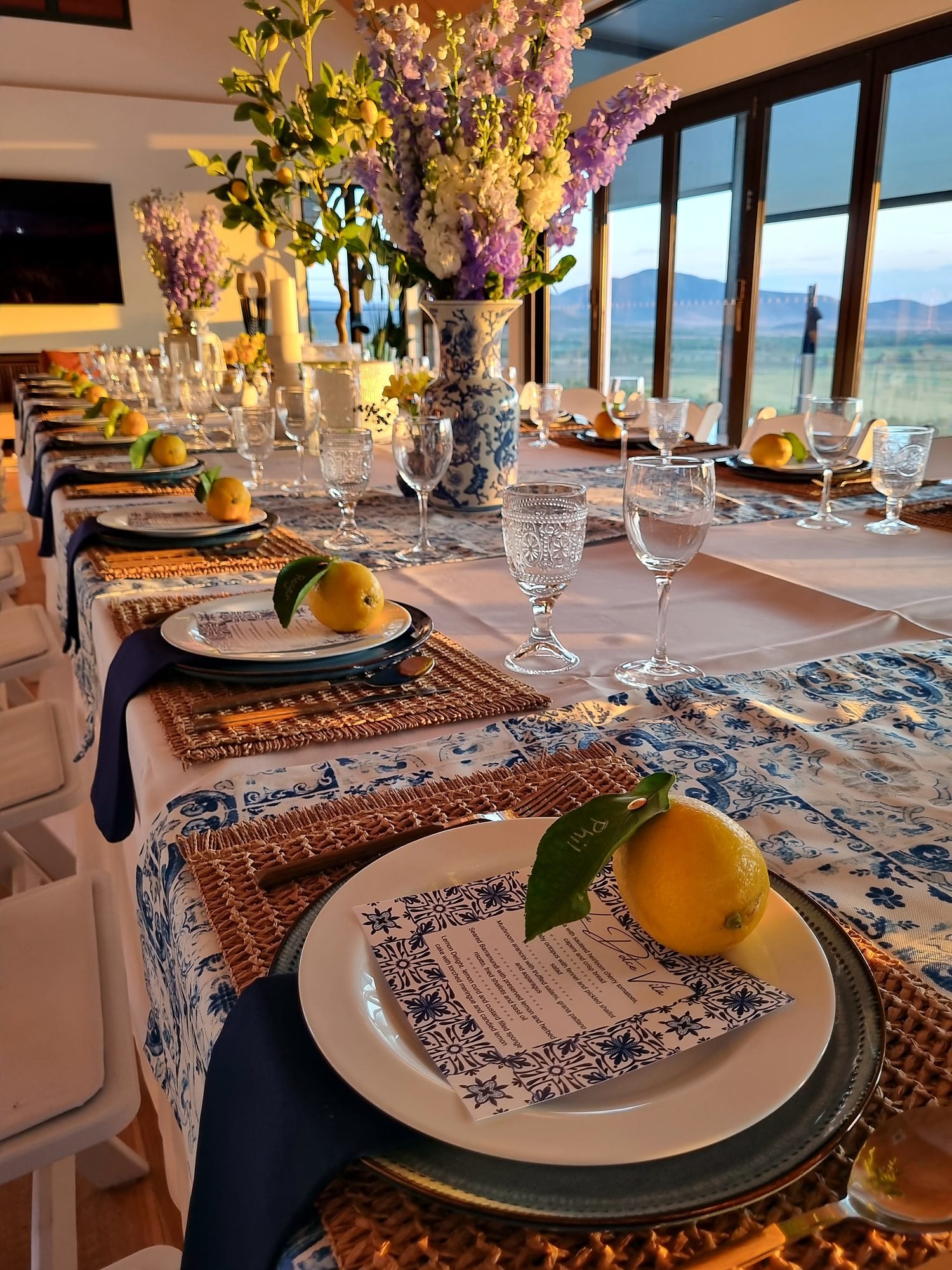 Wedding reception table dressed with florals, lemons and blue-and-white linen by the water