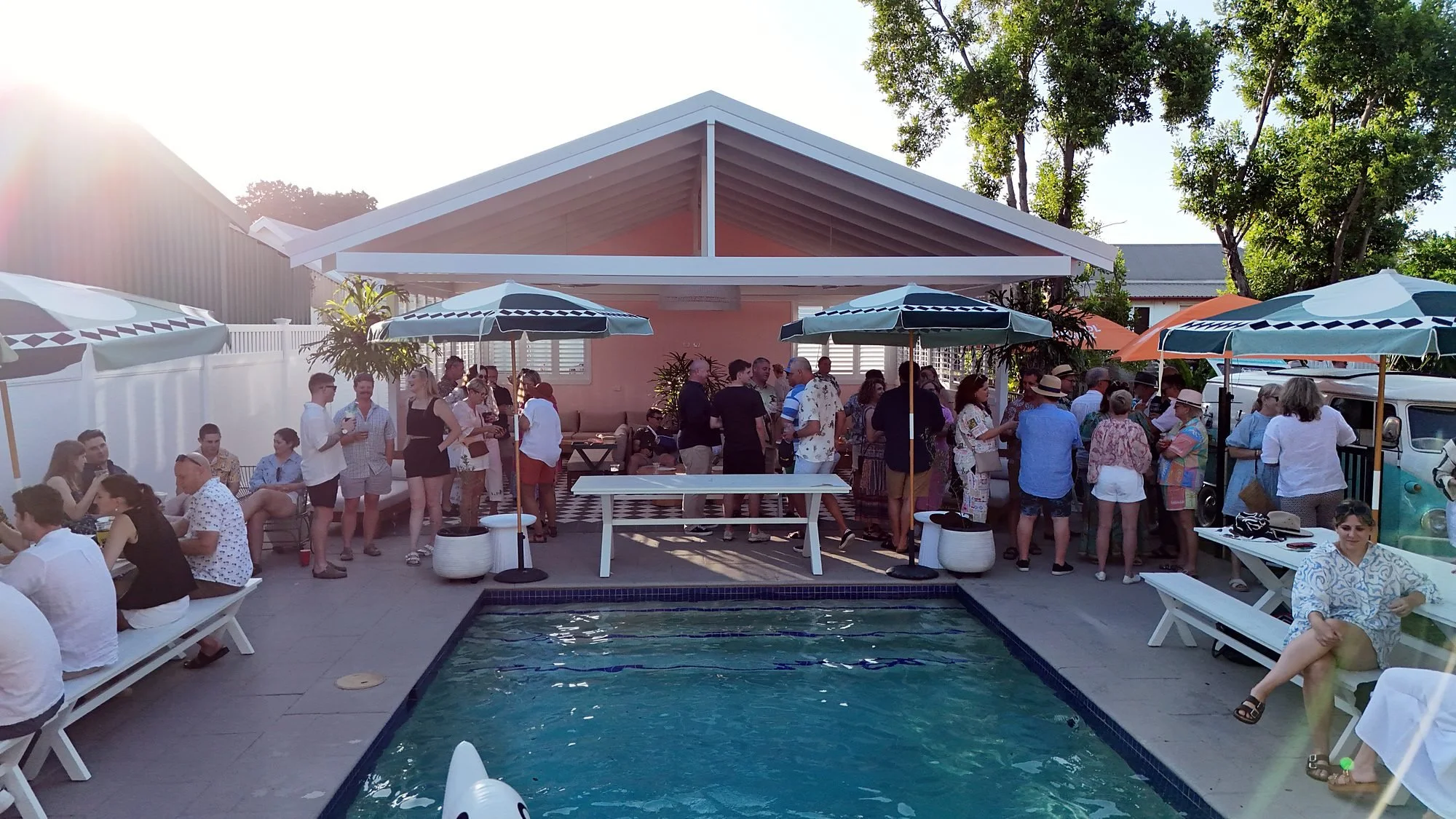 Guests mingling around a pool under striped umbrellas at a private celebration
