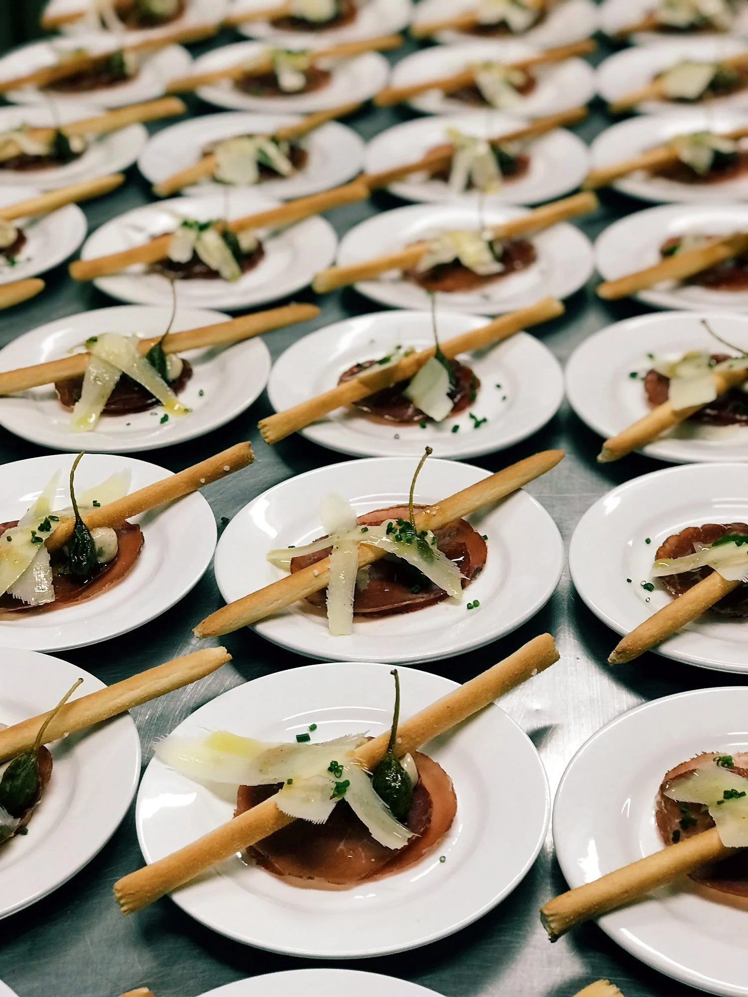 Rows of plated entrées with grissini and shaved parmesan, ready for service