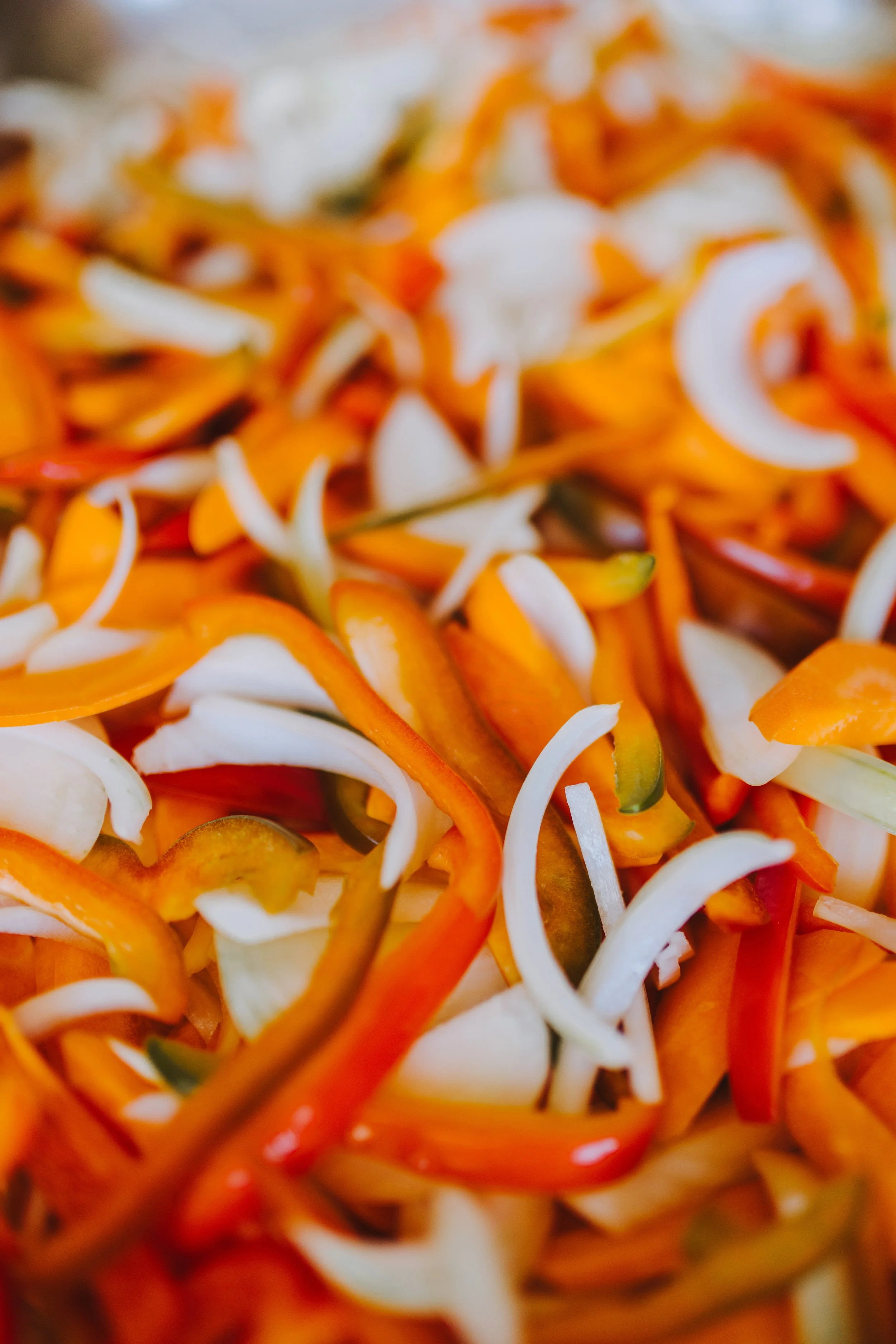 Close-up of shredded carrots, red bell peppers, green peppers, and sliced onions.