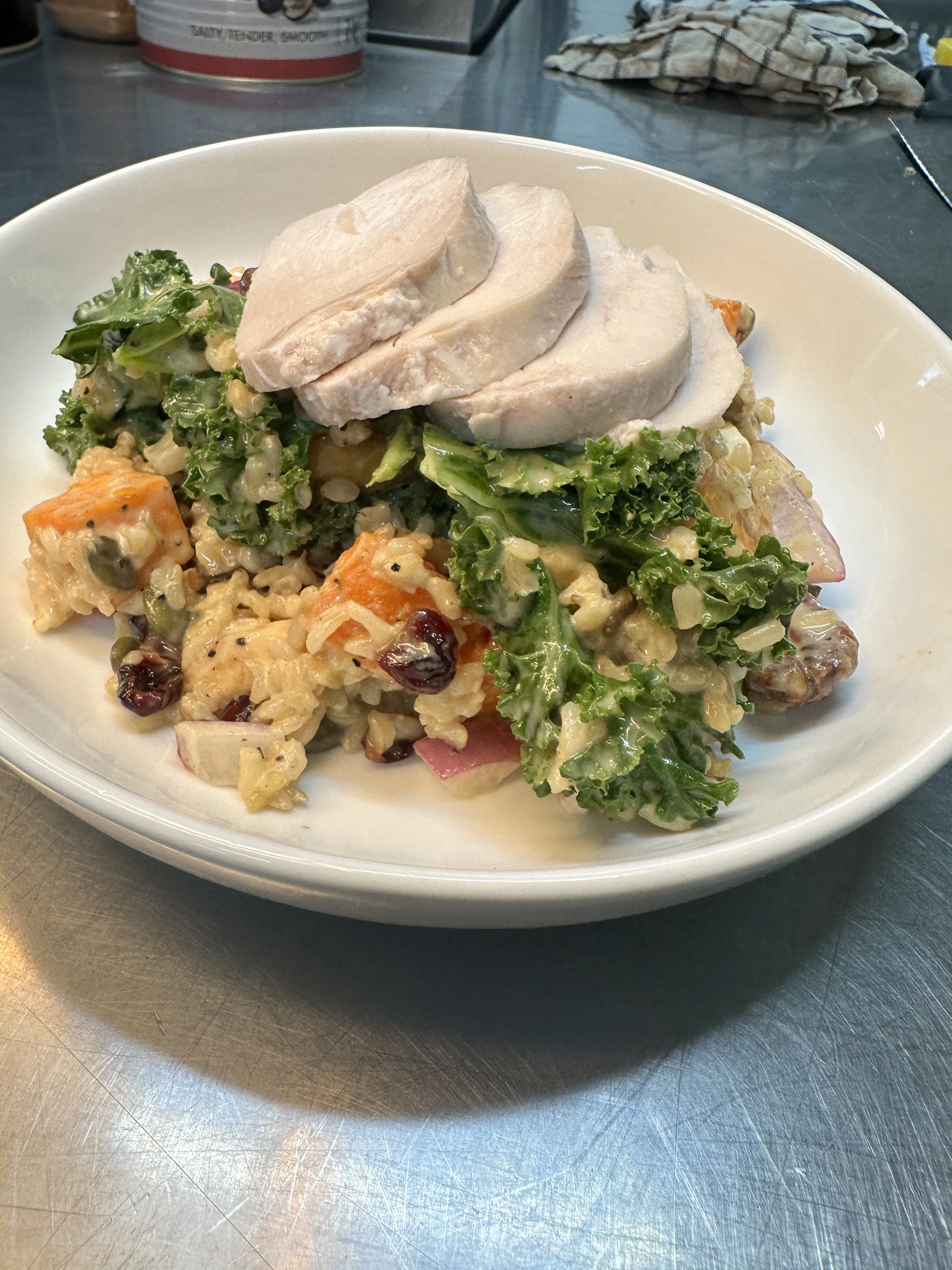 A bowl of salad topped with slices of cooked chicken breast on a metal table.