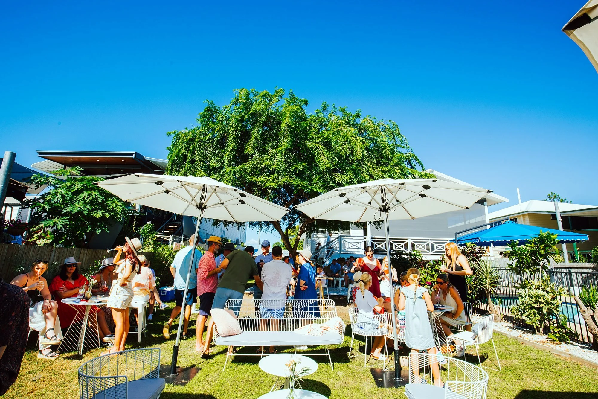 Guests mingling at an outdoor garden party styled with white umbrellas and lounges