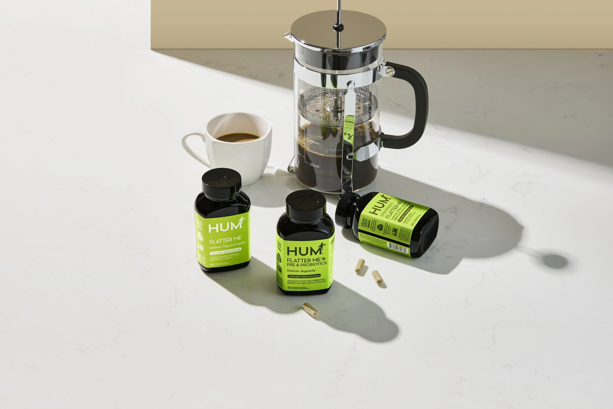 Los Angeles Set Designer, Art Director and Prop Stylist DANA KAPUSTIN featuring bright green bottles of HUM Nutrition's Flatter Me bottles on a white surface with French press and coffee cup behind bottles. 