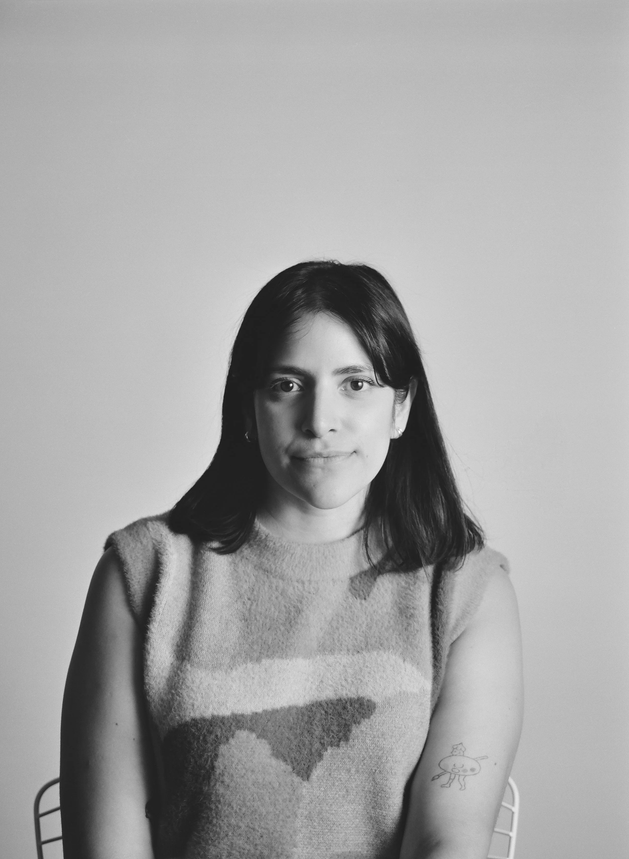 Black and white portrait of a woman with shoulder-length dark hair, wearing a sleeveless patterned top, sitting against a plain background.