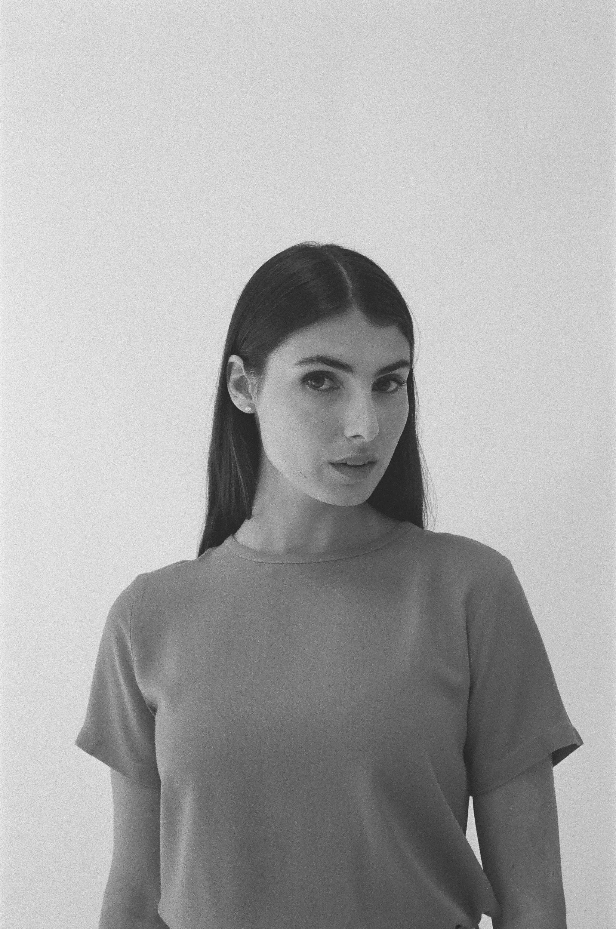 A young woman with long dark hair, wearing a casual T-shirt, posing against a plain background.