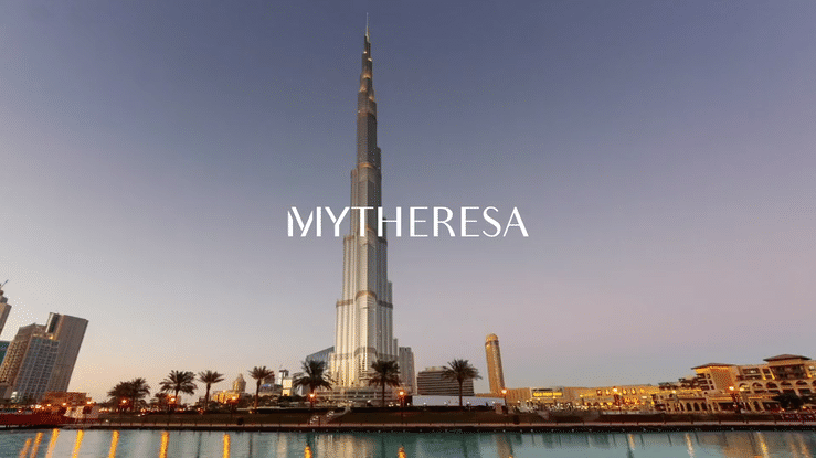 The Burj Khalifa skyscraper in Dubai with the title 'MyTheresa' overlaid, showing a waterfront view during sunset or sunrise.
