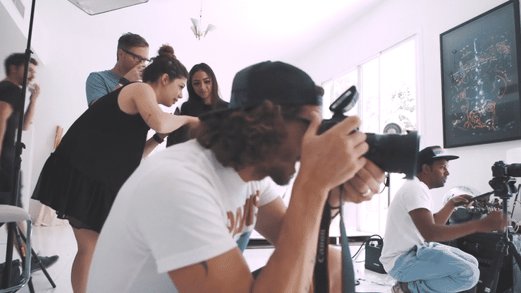 Group of young people engaged in a creative photoshoot or film shoot in a bright room with large windows and artwork.