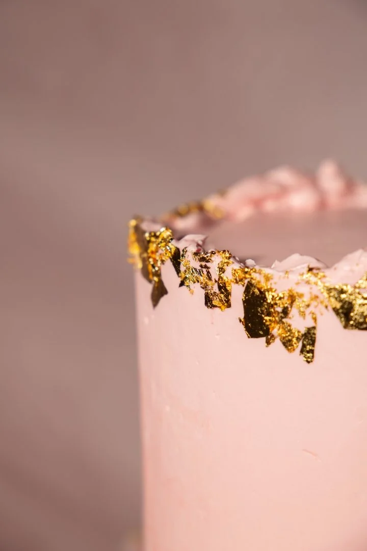 Close-up of a pink cake with gold leaf decorations on the top edge.