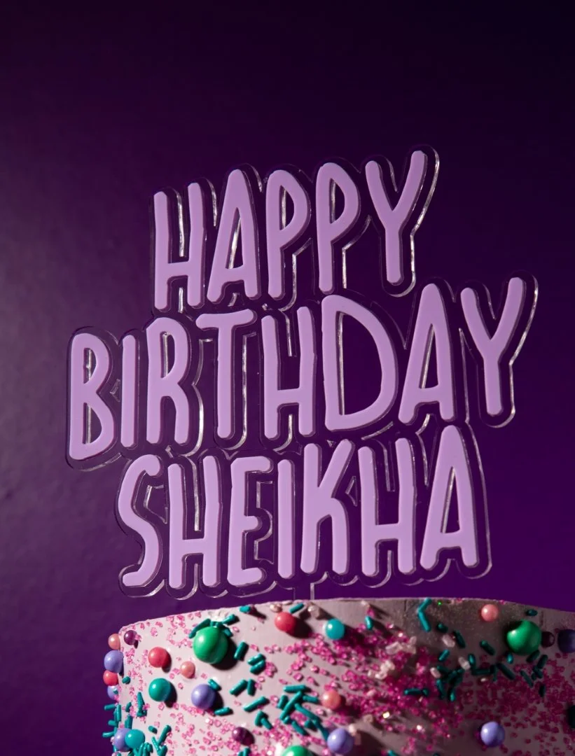 Purple neon sign that says "Happy Birthday Sheikha" with a decorated birthday cake at the bottom, topped with colorful sprinkles and candies.