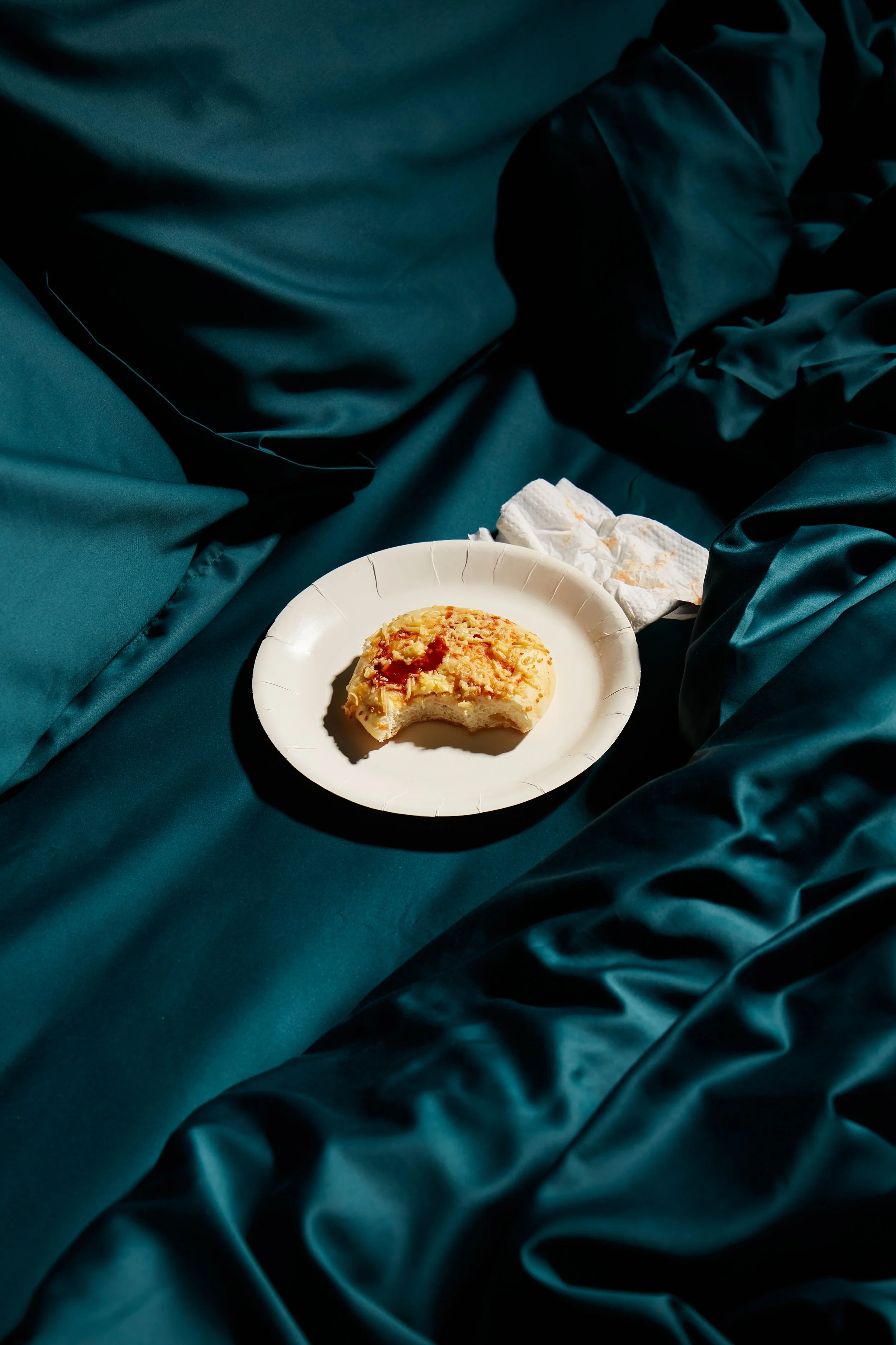 A partially eaten piece of cake on a paper plate, resting on dark teal satin sheets.