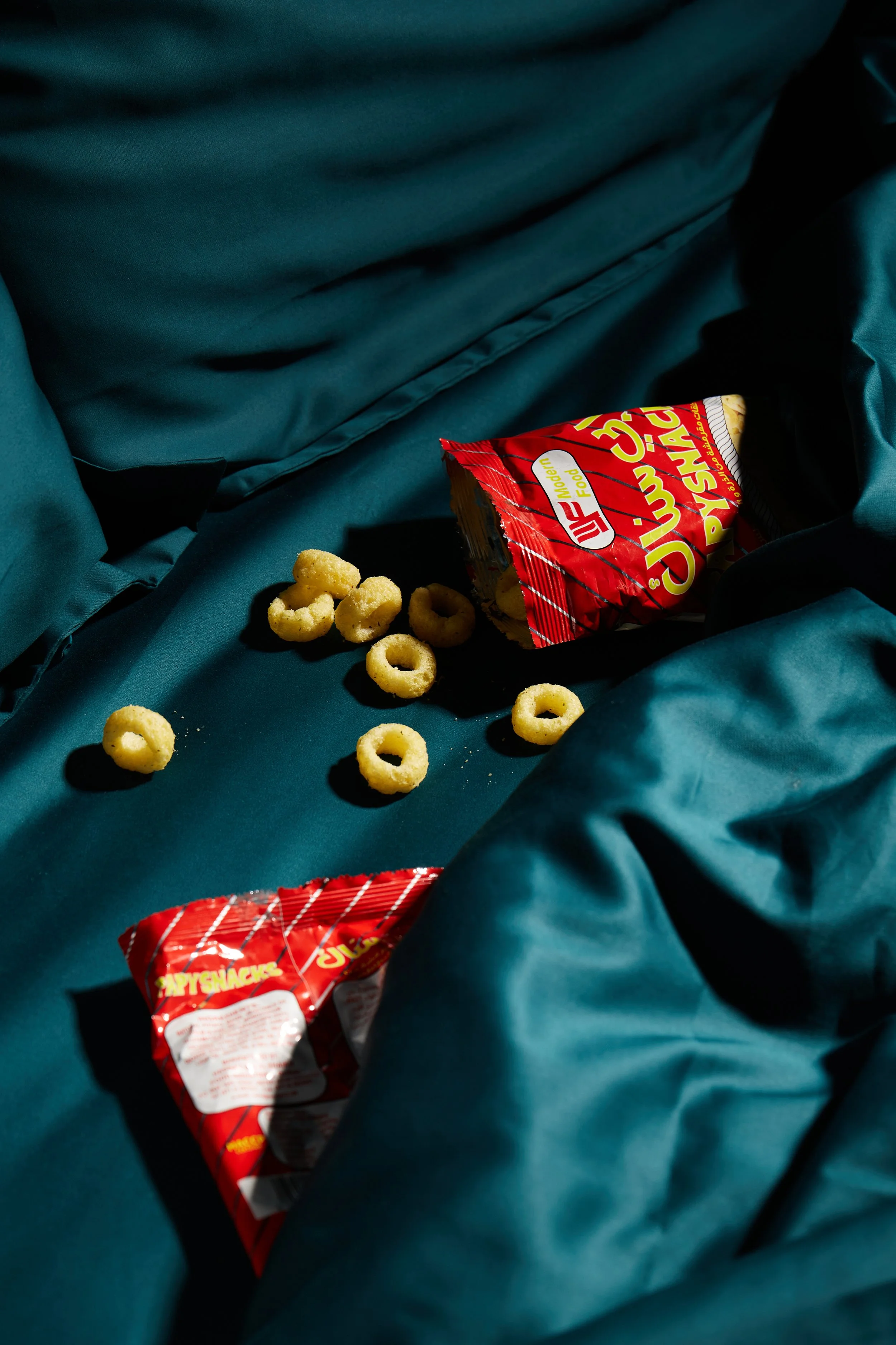Open bag of cheese puff snacks and scattered cheese puffs on a teal fabric surface.