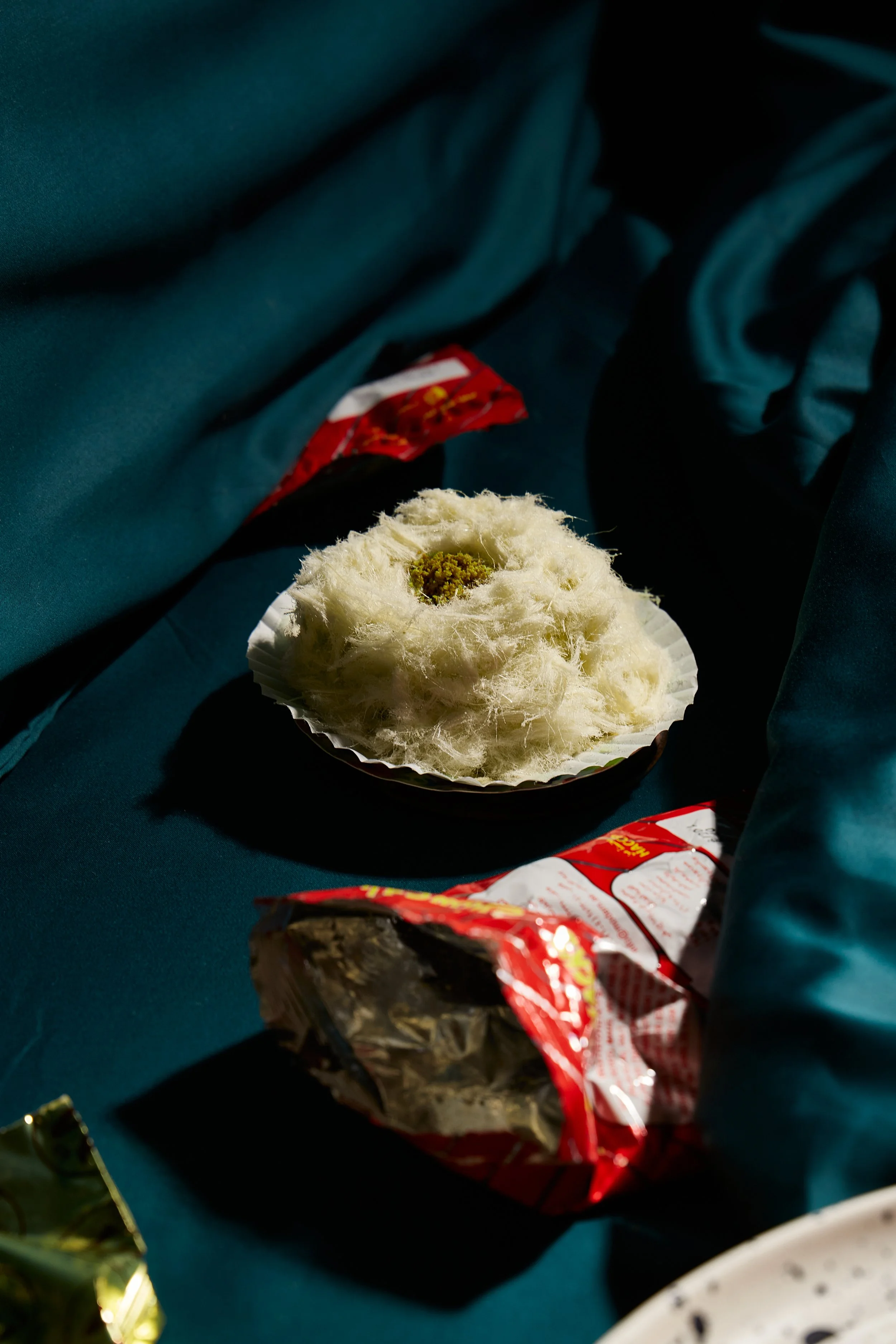 A steamed bun with a yellow filling inside, placed on a paper plate, next to a partially opened red snack bag on a dark blue picnic table.