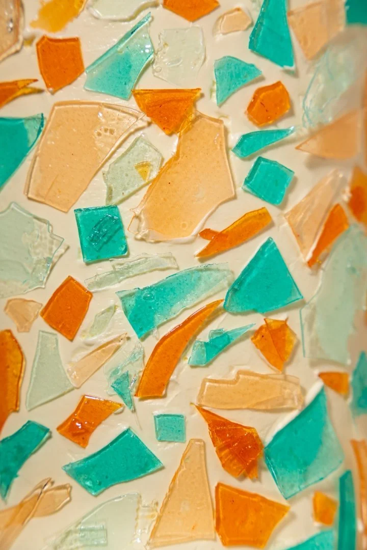 Colorful shards of glass in shades of orange, beige, light green, and teal scattered on a white surface.
