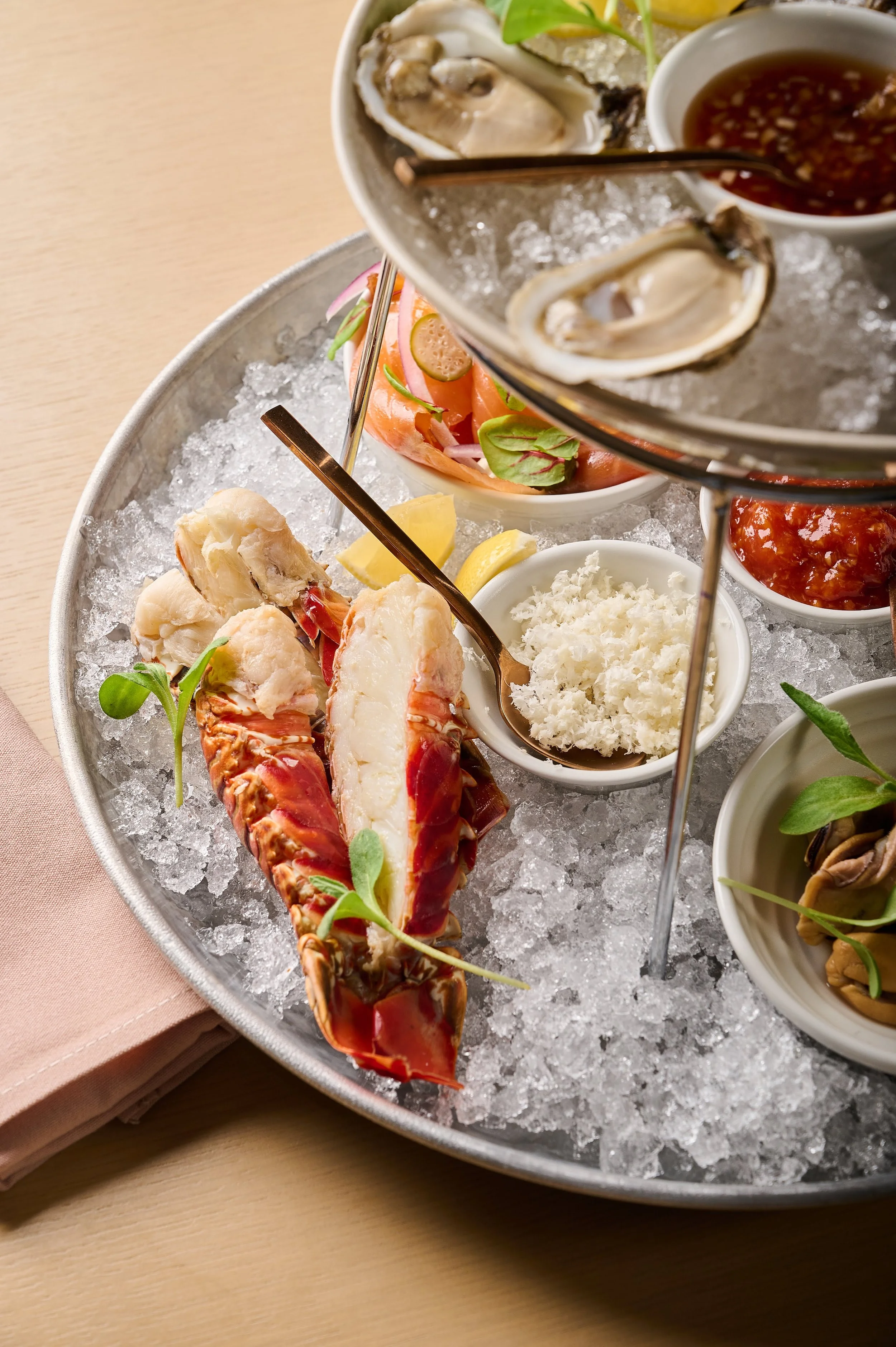 Lobster tail and oysters on a bed of ice with various dipping sauces and garnishes.