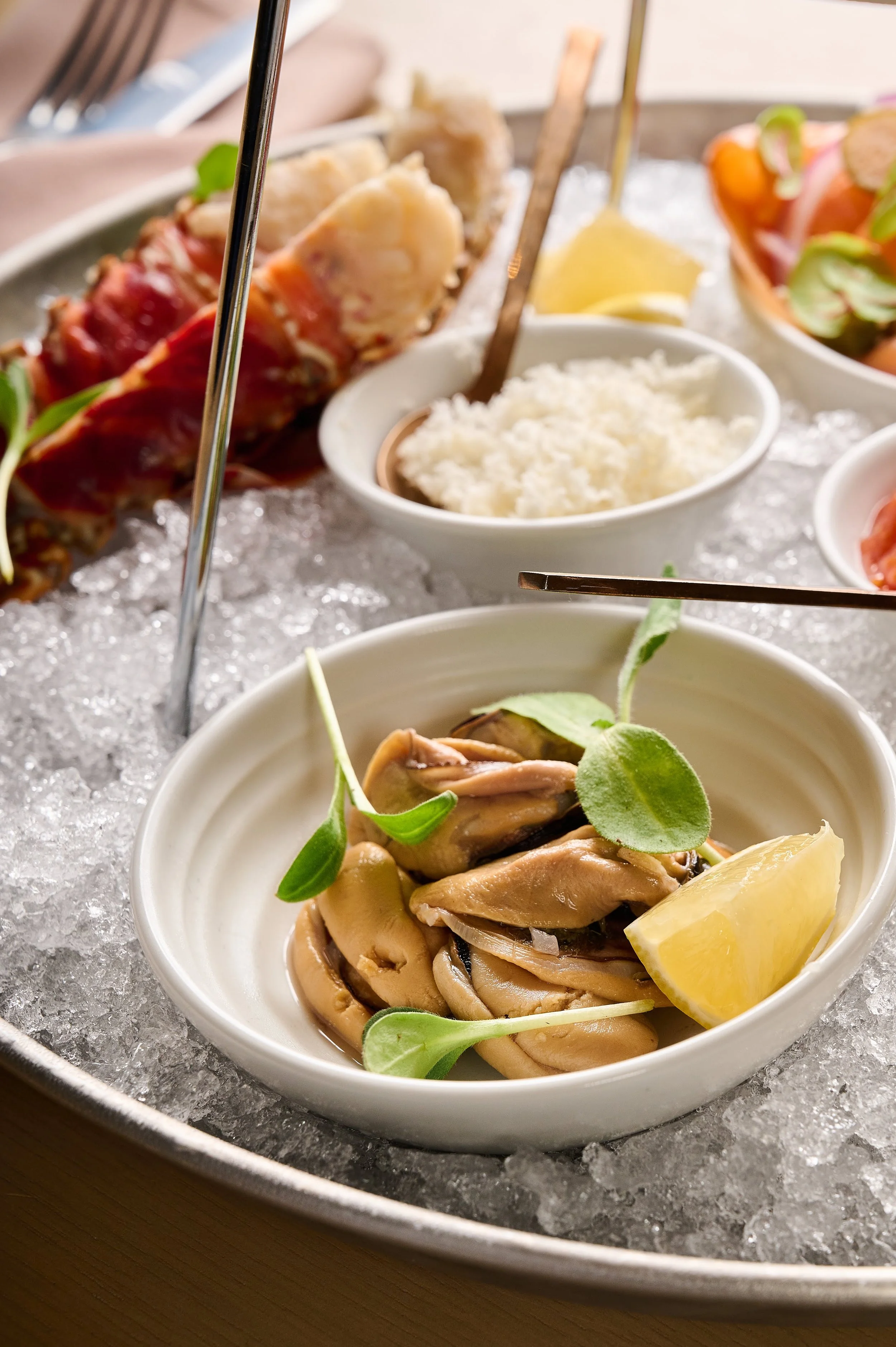A close-up of a seafood dish with mussels, garnished with green herbs and lemon wedge, served on a bed of ice.