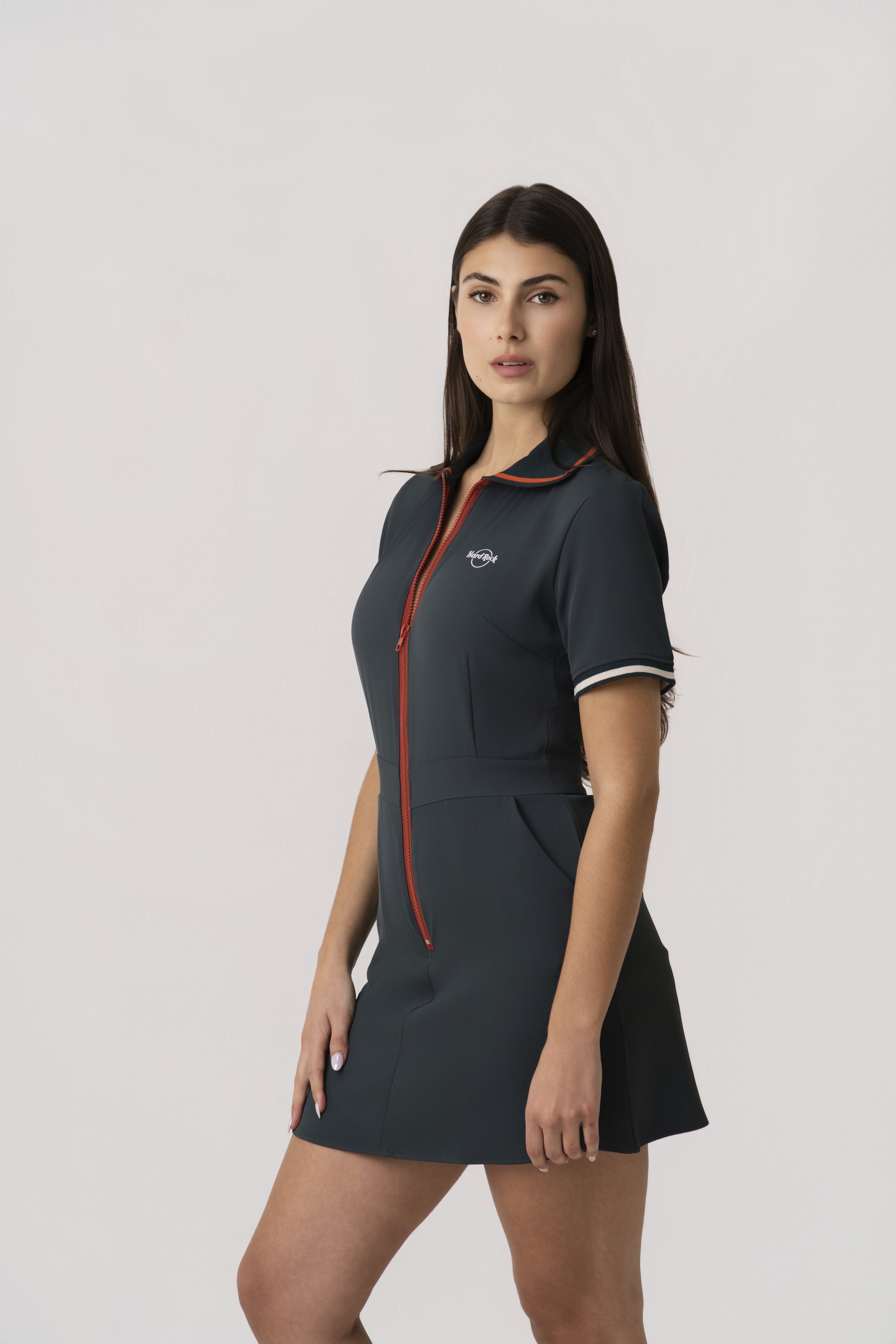 A female model wearing a black dress with a front zipper, standing against a plain white background.