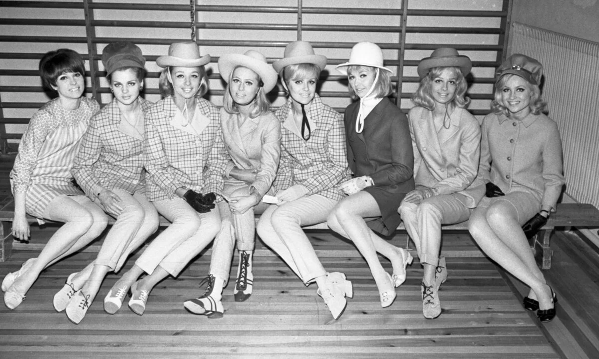 Sex kvinnor på en bänk framför en ribbstol, iförda hattar och rutiga kavajer i lätt cowboystil.