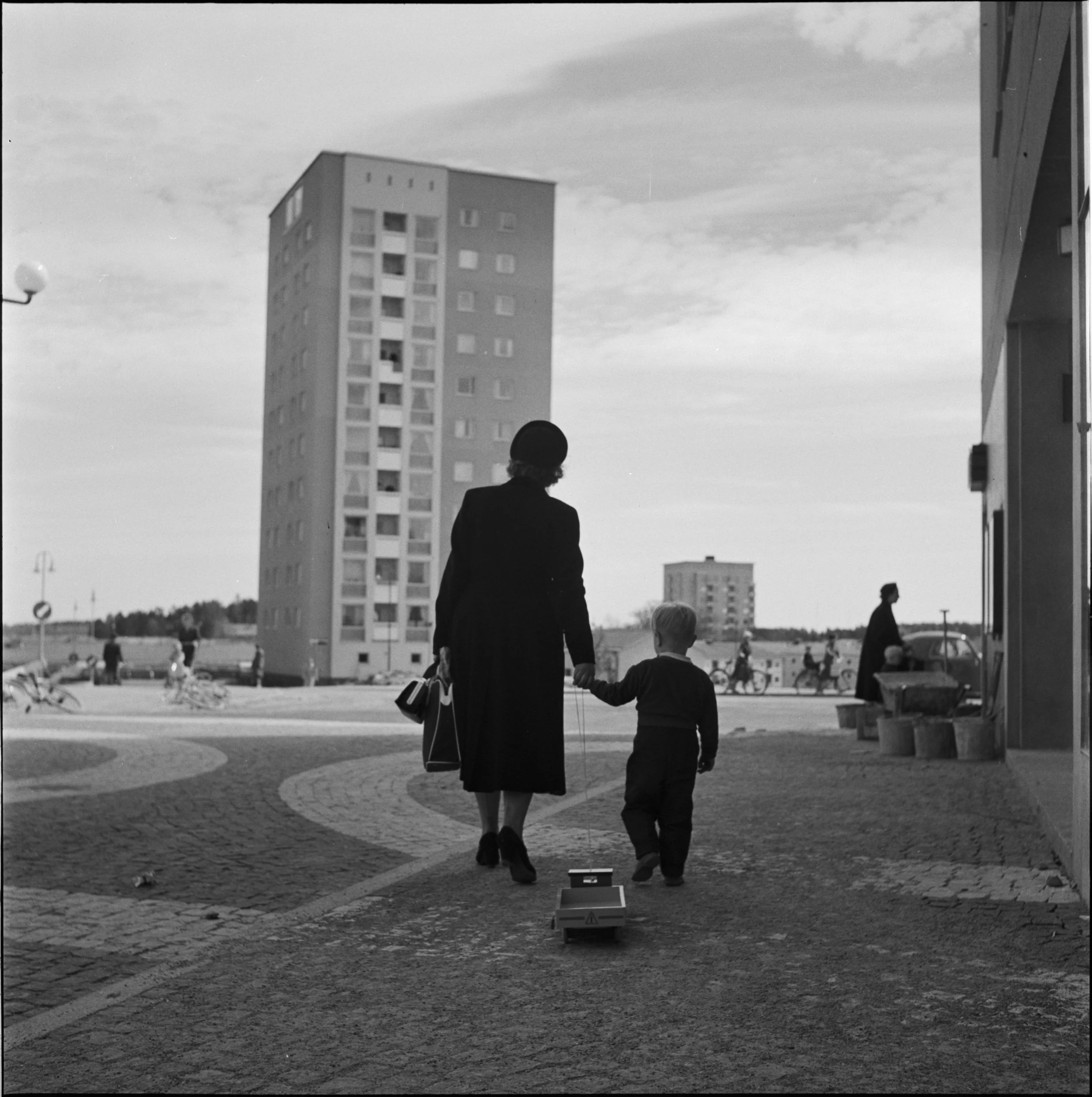 Mamma och son promenerar hand i hand i Vällingby med höghus i förgrunden.