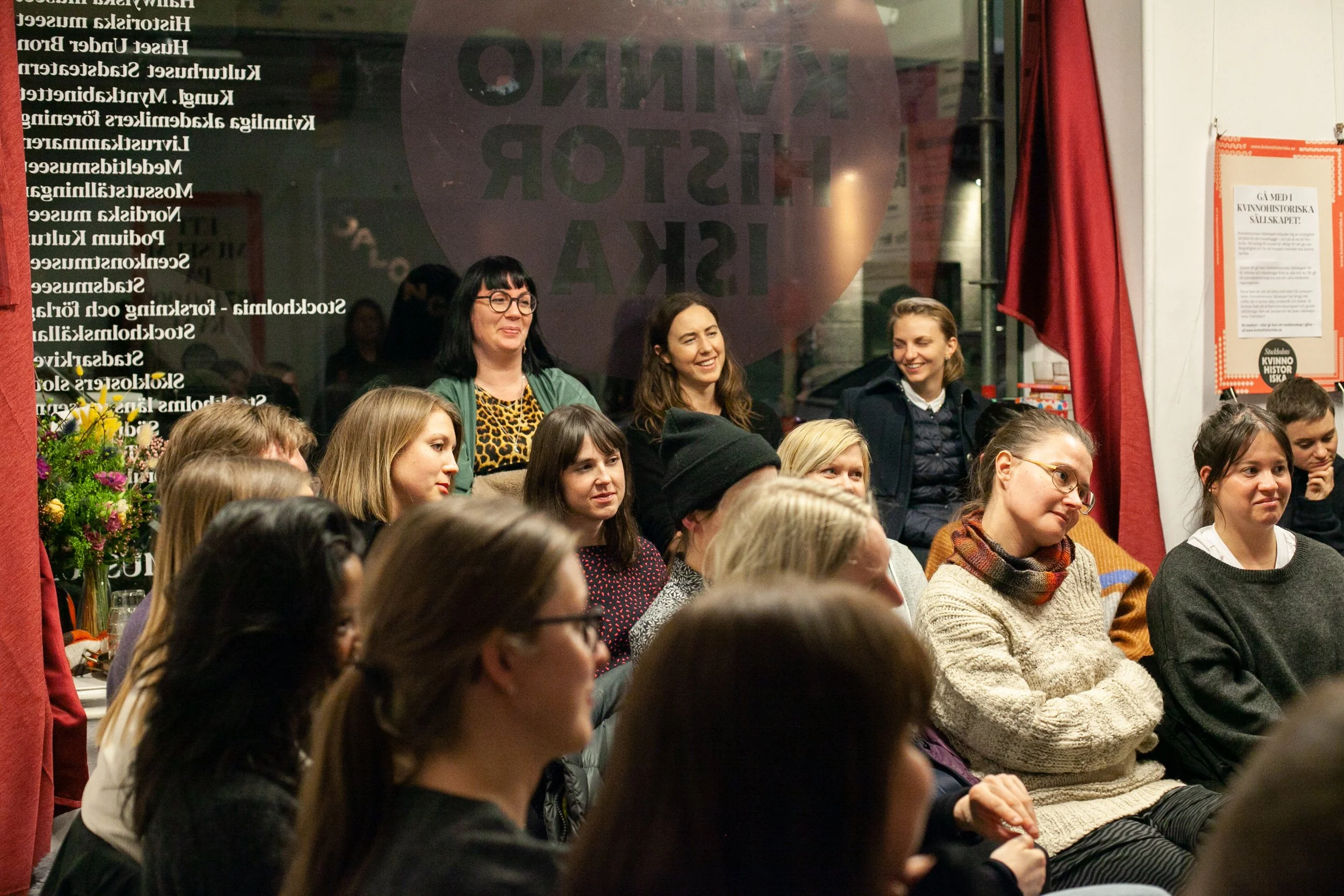 Personer samlade i lokalen på Hökens gata, sitter i fönstret och på stolar och lyssnar.