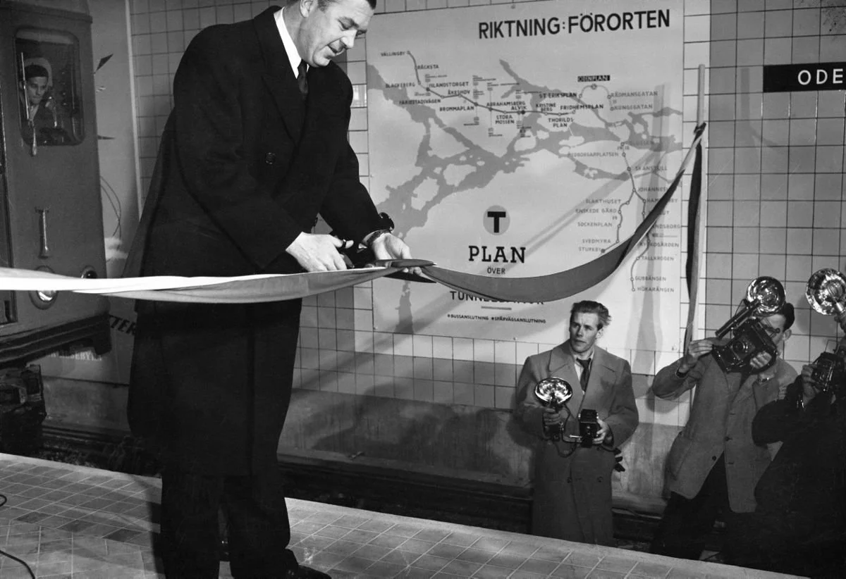 Prins Bertil klipper ett band med en stor sax, på spåret står fotografer och fotograferar.