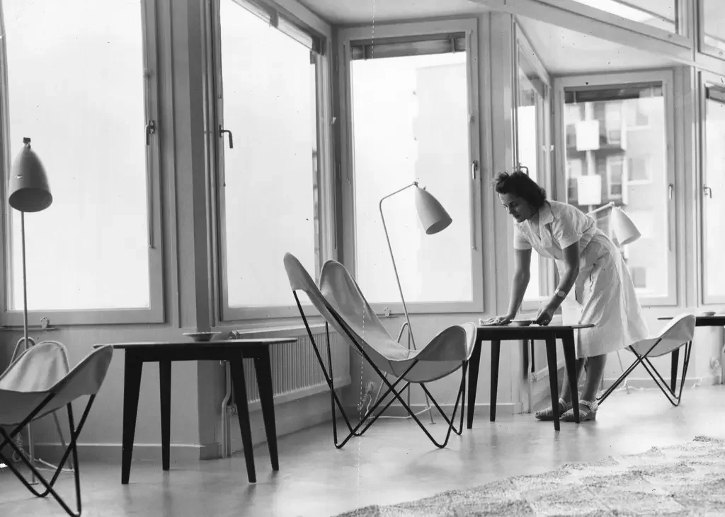 Kvinna dukar vid ett bord vid fladdermusfotölj och lampa på "Lunchbaren" i Vällingby.