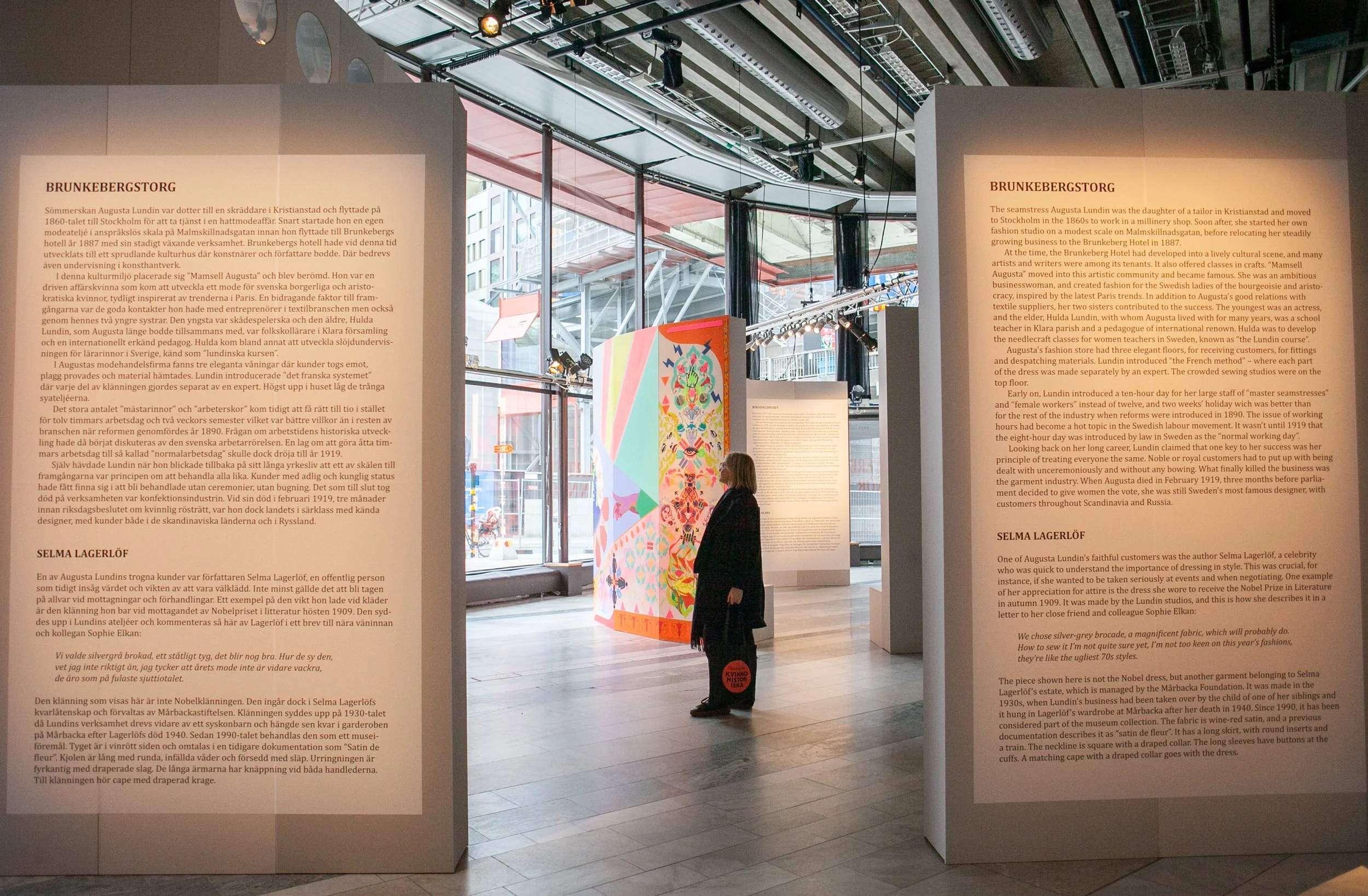 En person står och tittar i utställningen, närmast syns höga väggar med text om Brunkebergstorg och Selma Lagerlöf.