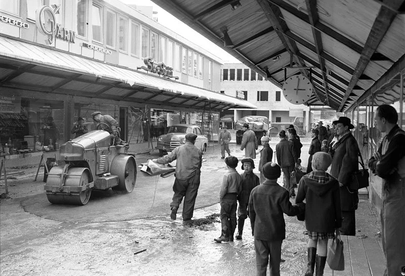 Barn, vuxna besökare i Vällingby centrum samsas med byggarbetare som lägger asfalt i centrum dagen innan invigningen.