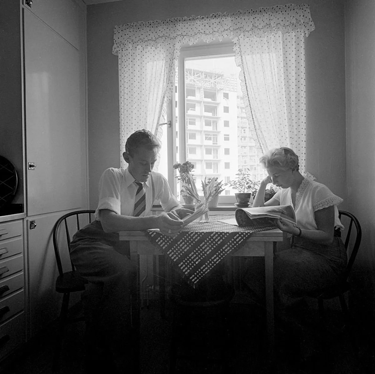 En man och kvinna nedböjda över tidningar vid ett köksbord