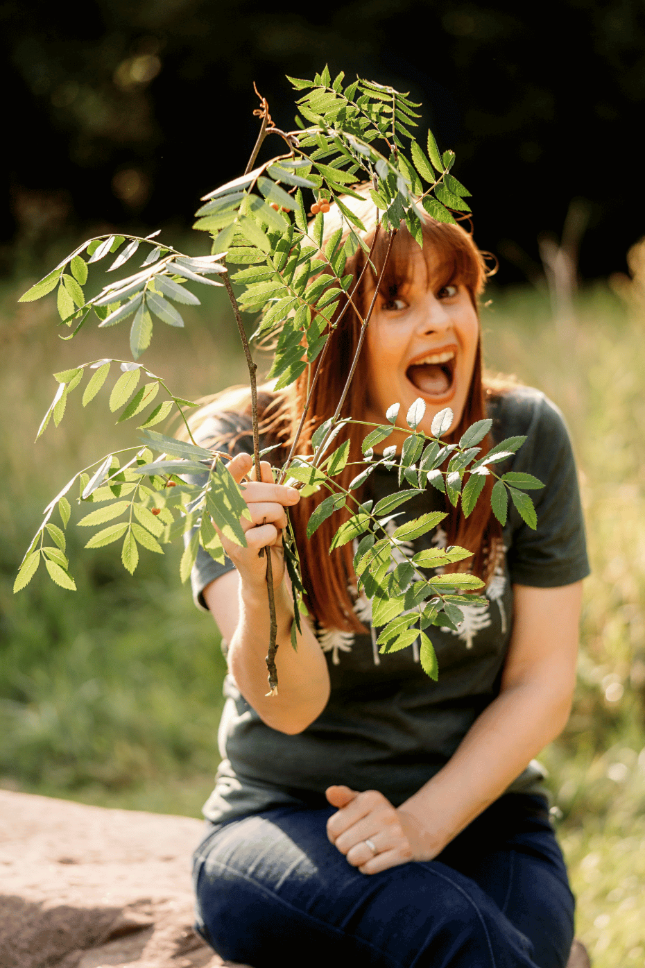 Kath's doing a happy face as she peeps out between some leafy little branches she's found in the woods.