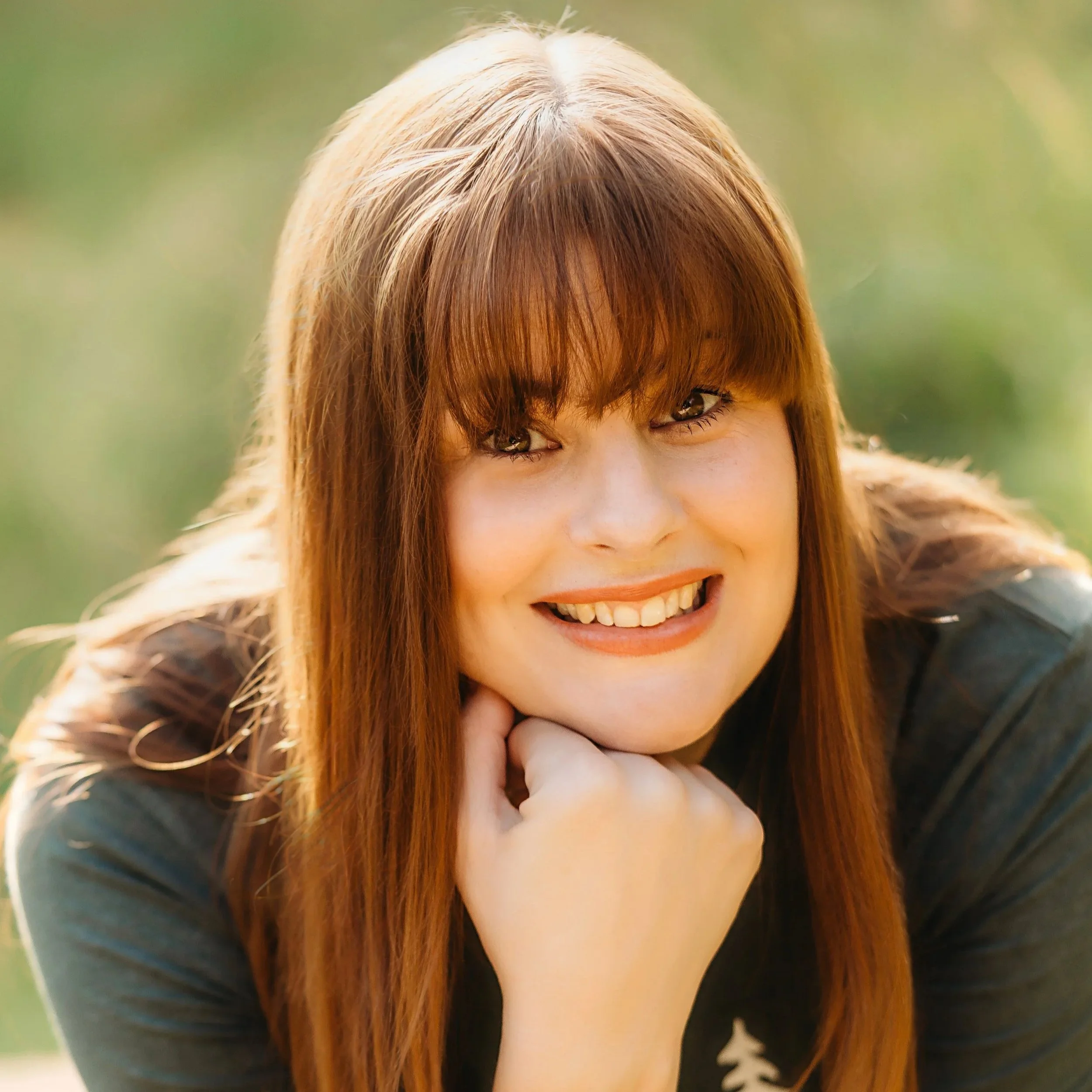 Kath looks up into the camera smiling. She has a windswept fringe and she's resting her chin on her hand.
