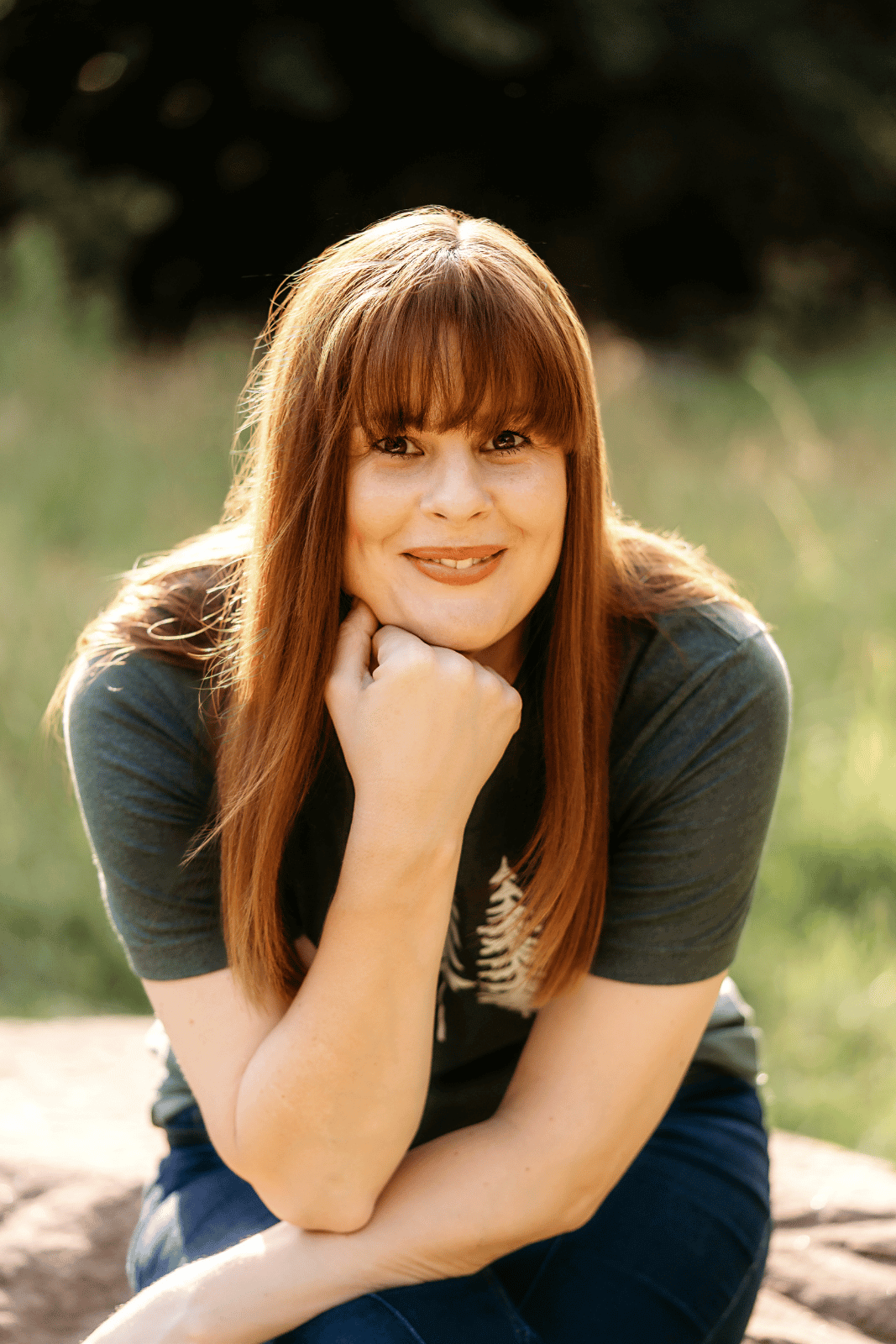 Kath is resting her chin on her hand and looking at the camera. She's wearing a tree t-shirt.