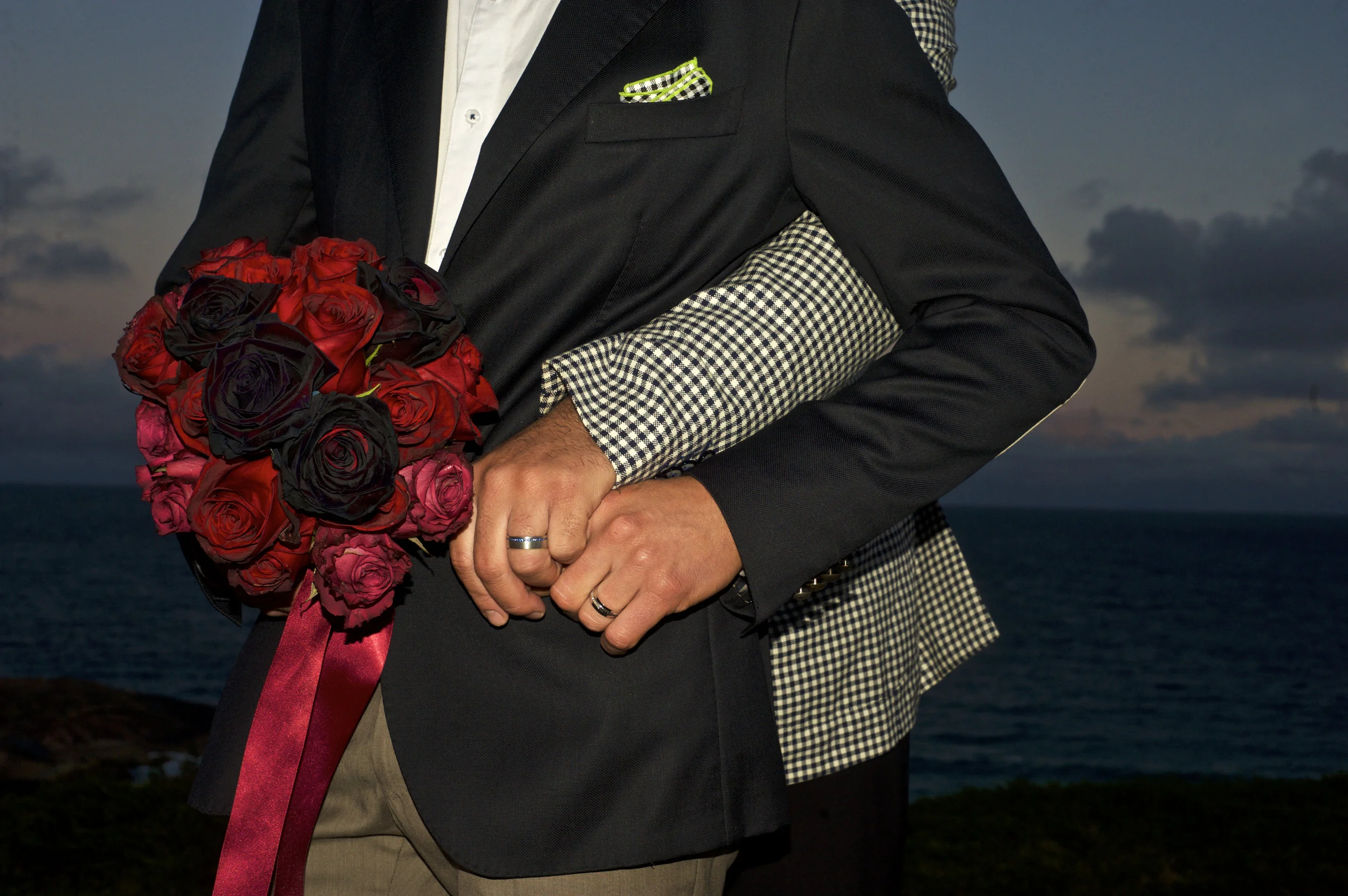 married couple holding hands by the beach side holding bouquet of flowers sunset after wedding