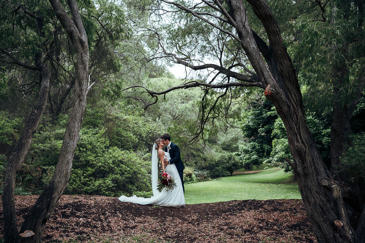 bride and groom holding bouquet flowers kissing under a tree