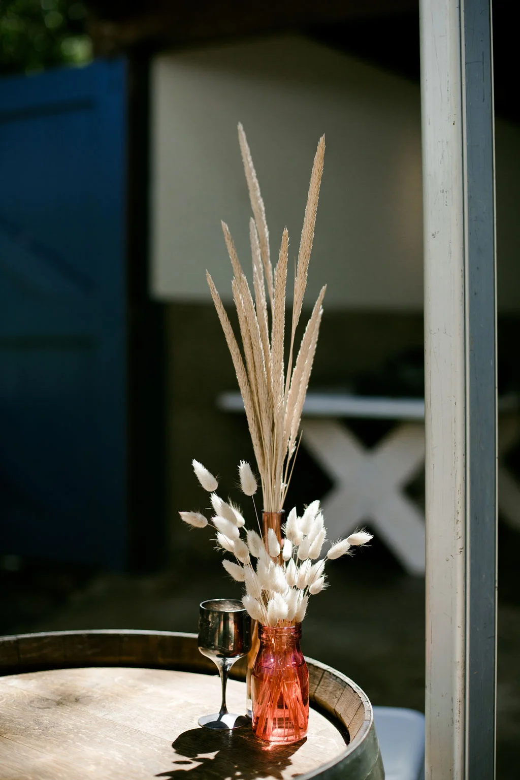 glass vase with beautiful plants on a barrel with metallic wine glass