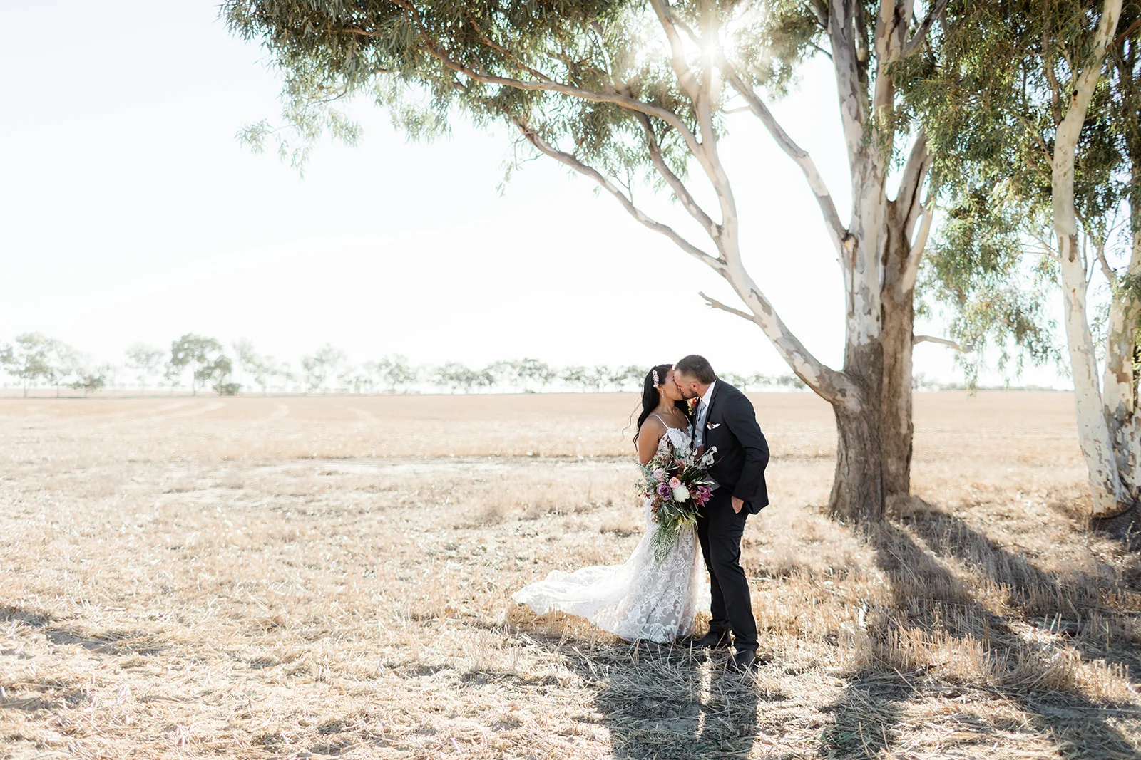 bride and bride groom kissing outdoors under a tree on wedding day