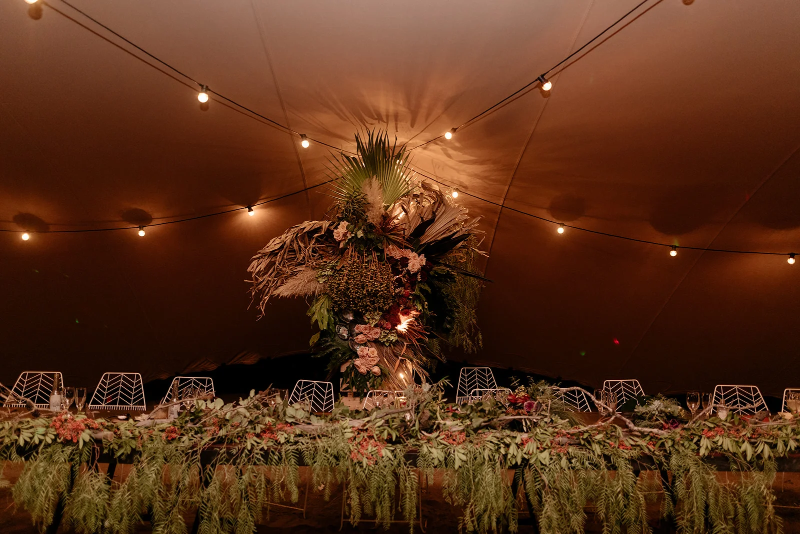 wedding sitting arrangement in a tent with chairs lighting and flowers