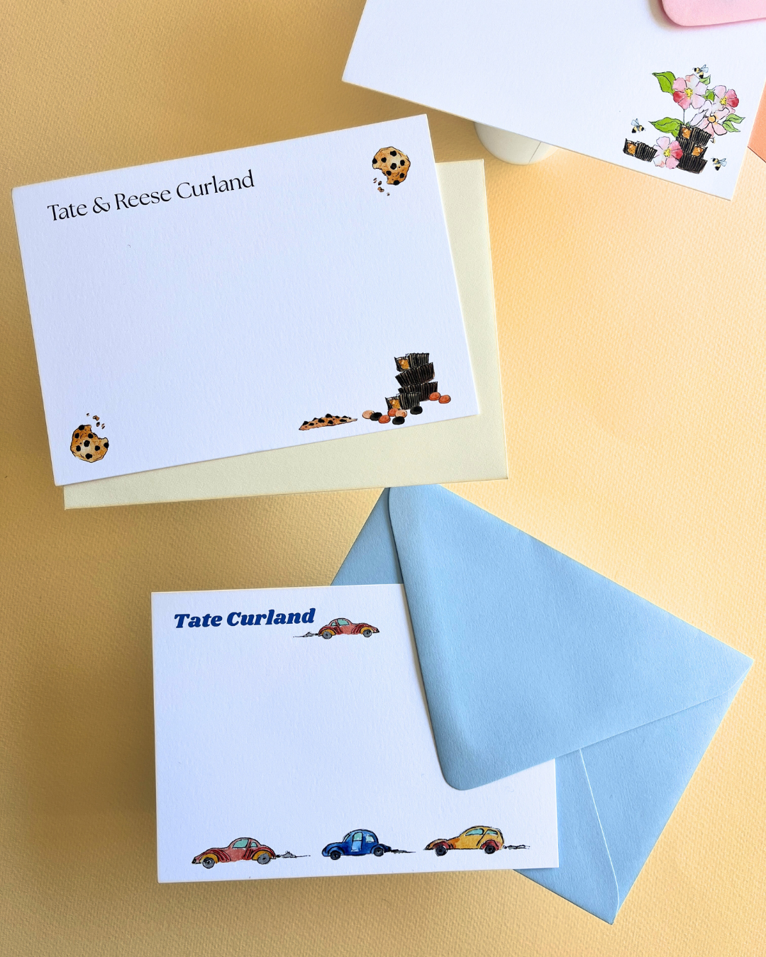 Multiple personalized notecards and envelopes with colorful illustrations, including cars, flowers, cookies, and a chocolate bar, placed on a yellow background.