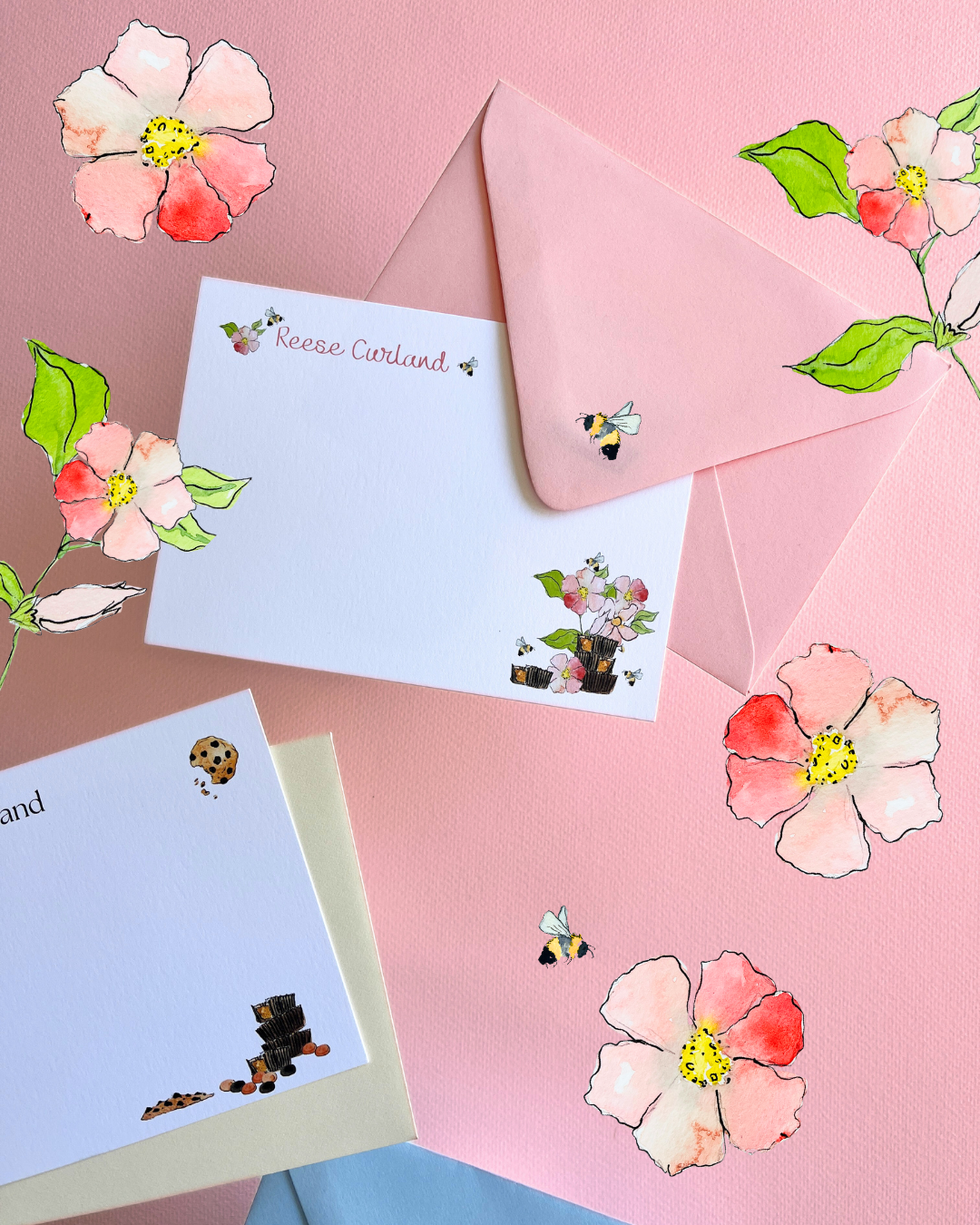 Pink and white floral-themed stationery set with a white card, pink envelope, and decorative floral stickers with bees and a ladybug, arranged on a pink background.