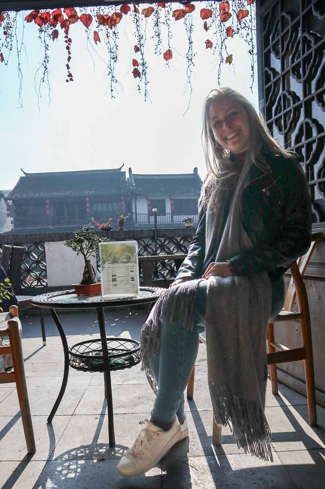 Mrs.Timcsi (Csürös Tímea) in a casual city outfit enjoying the sunshine in Zhujiajiao, near Shanghai on sunny tea houses balcony. Autmun wine leaves hanging from the door frame and traditional chinese buildings fill out the background.