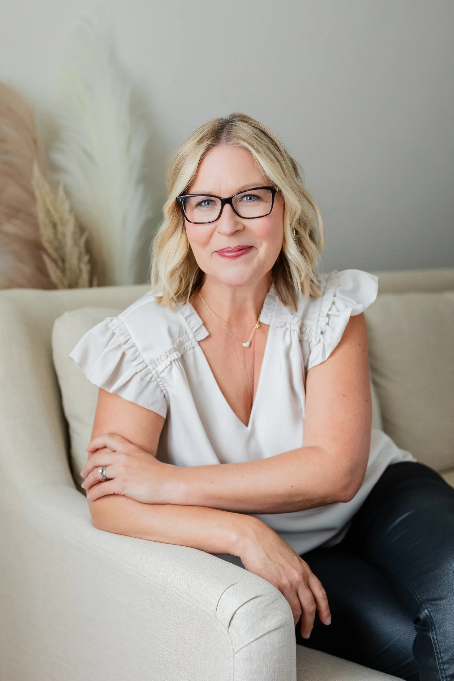 Ann seated on a light linen sofa, wearing a light ivory top, in natural light during her 50 Over 50 portrait session in Houston.