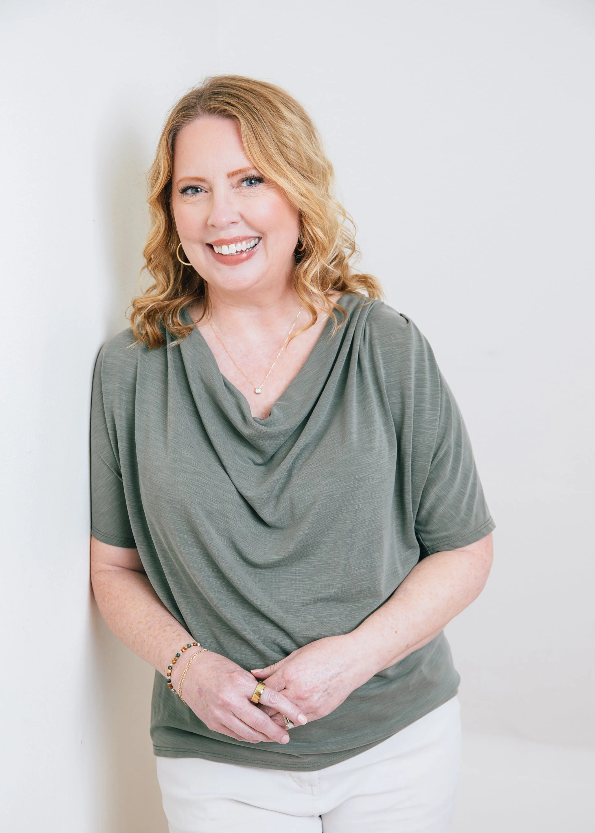 Woman with red hair poses in a green top and white pants for a beauty photo shoot for women over 50 in Amanda Faucett Photography's Houston studio.